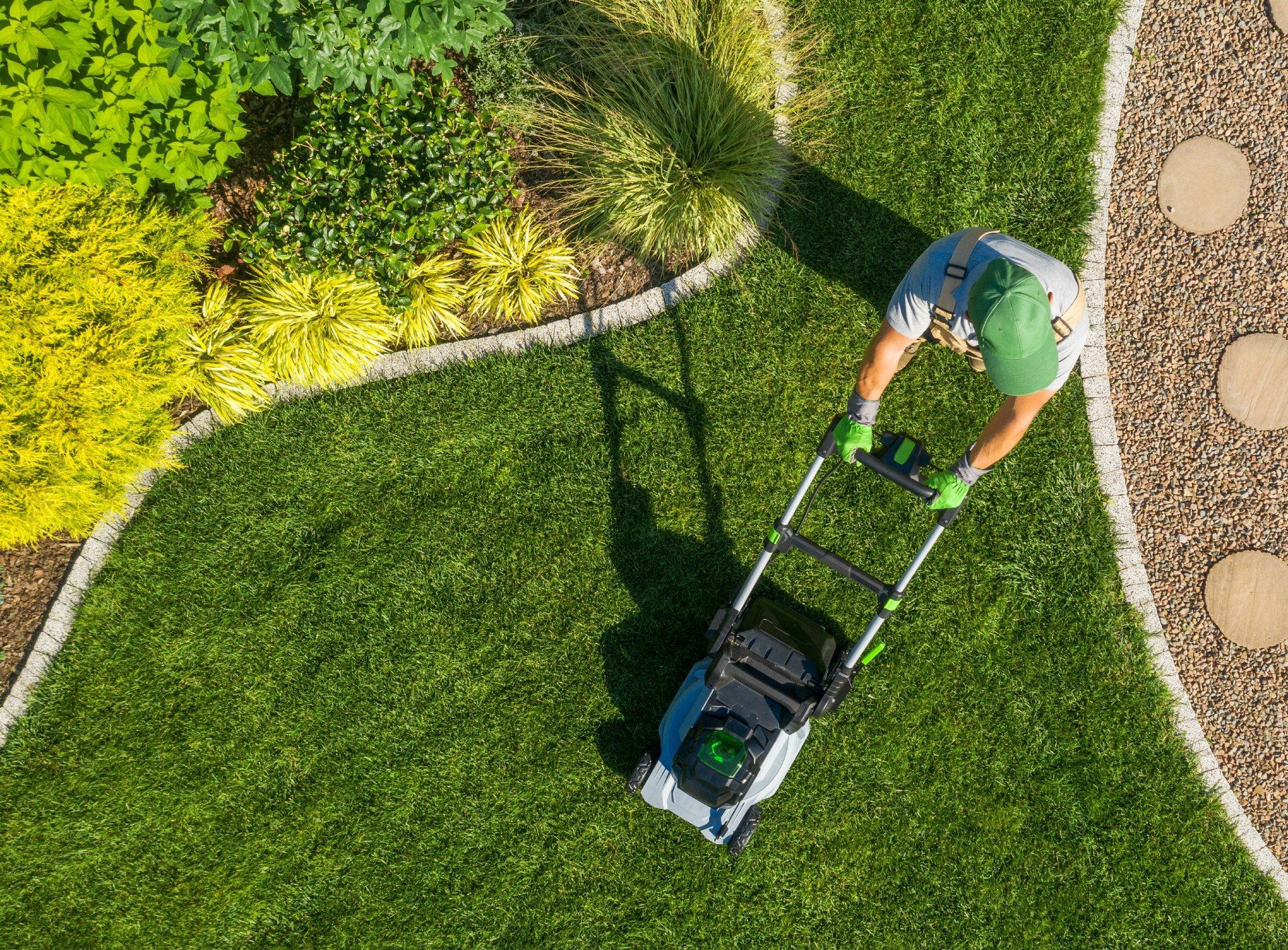 Person mowing a green lawn with an electric mower; overhead shot.