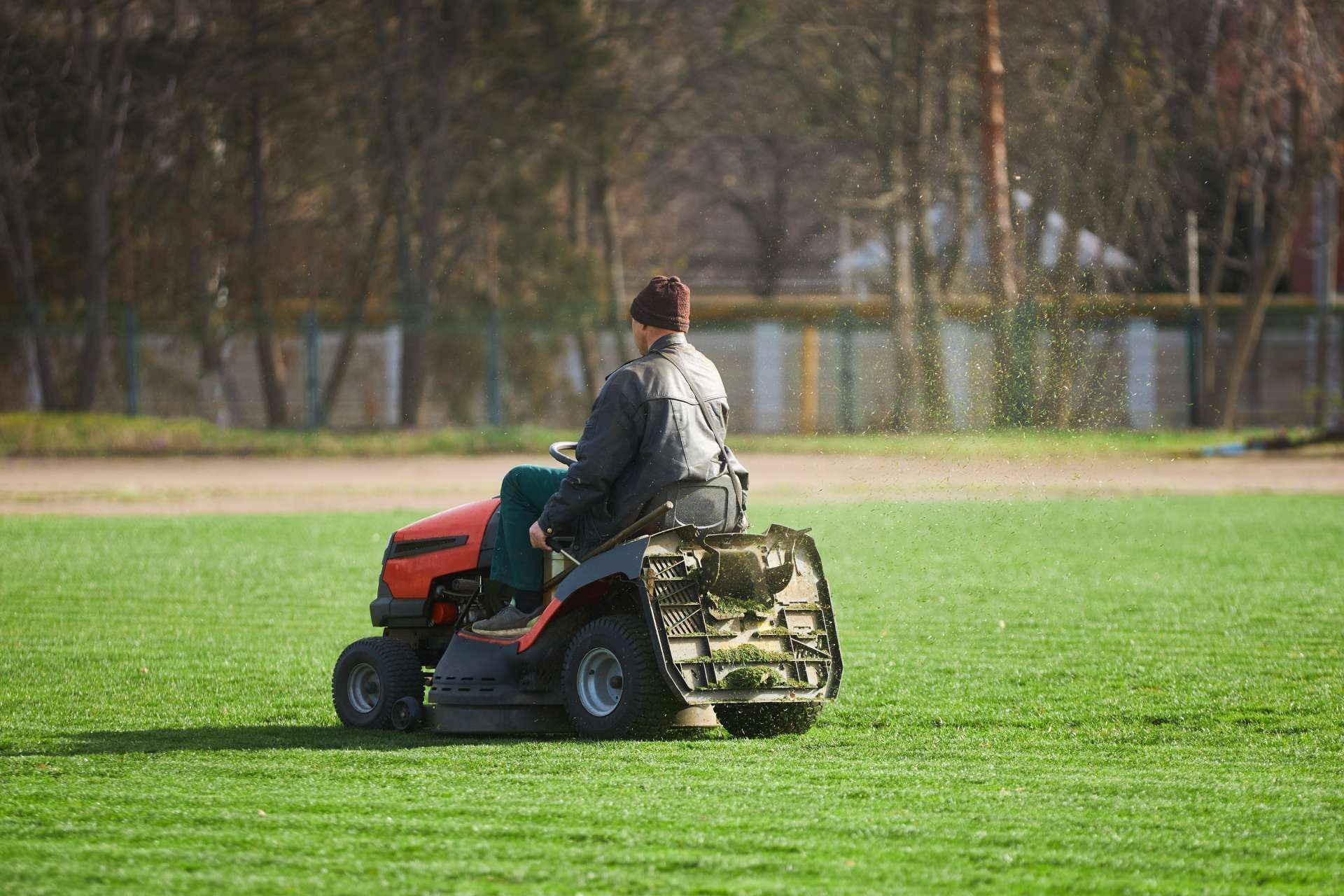 Person riding a red and black lawn tractor, mowing a green lawn.