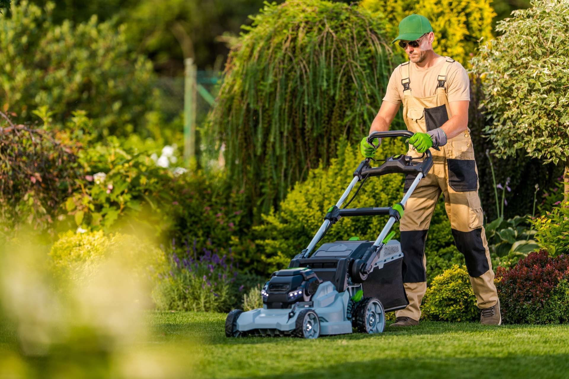 Man mowing a green lawn with a gray and black mower, in a sunny garden.