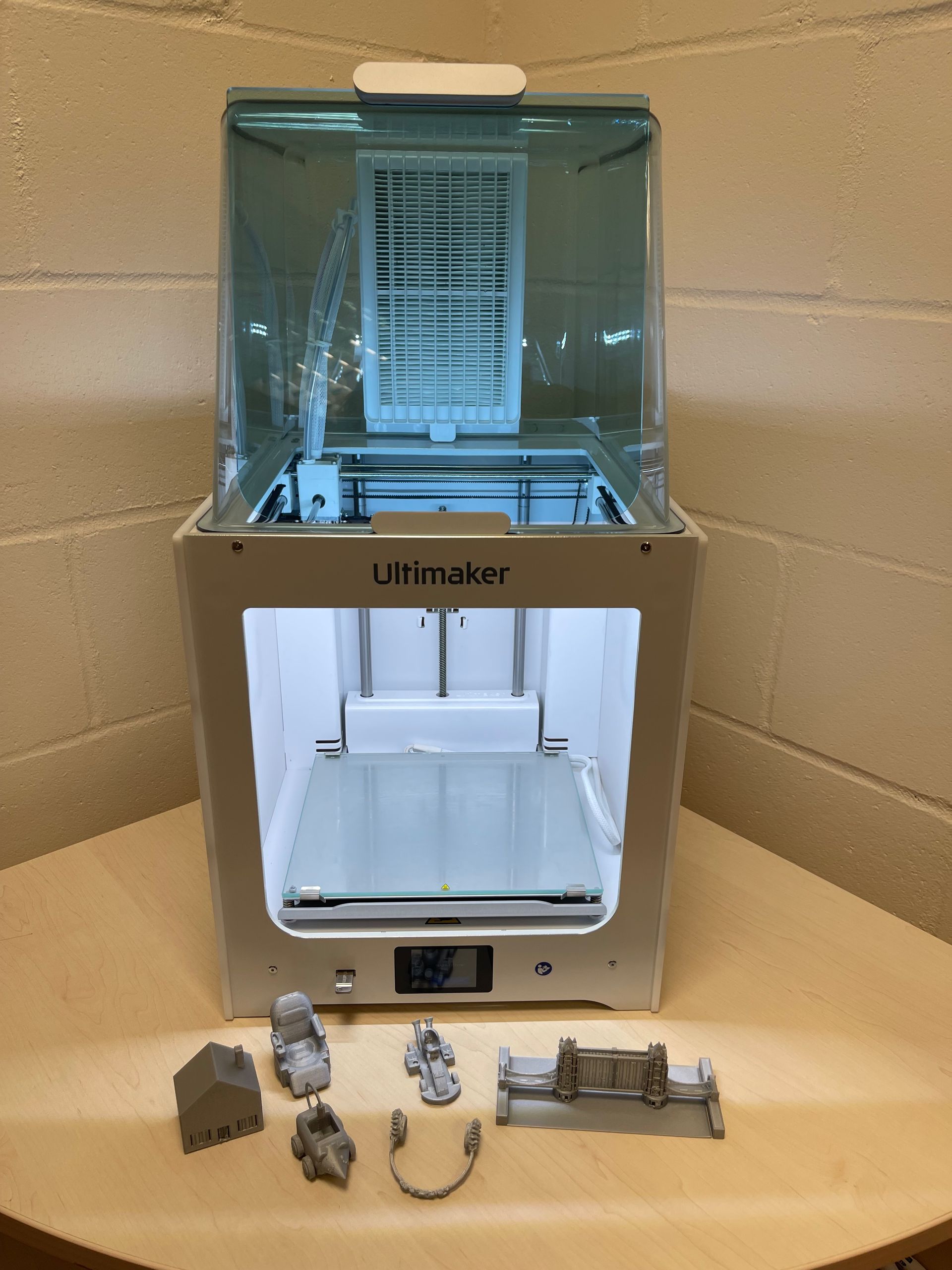Ultimaker 3D printer with printed gray objects on a wooden table.