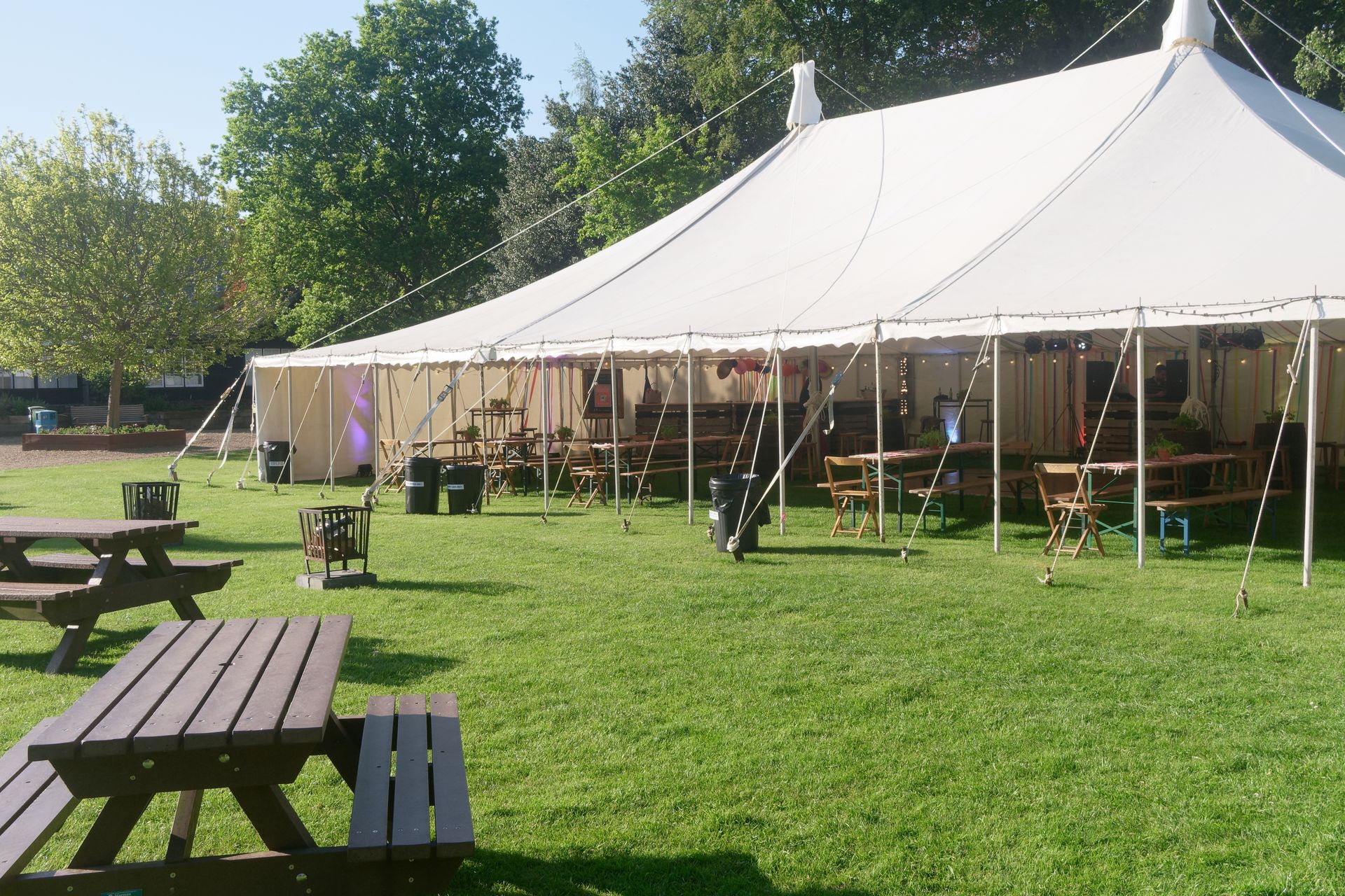 White tent on a grassy lawn with picnic tables, trees, and clear sky.