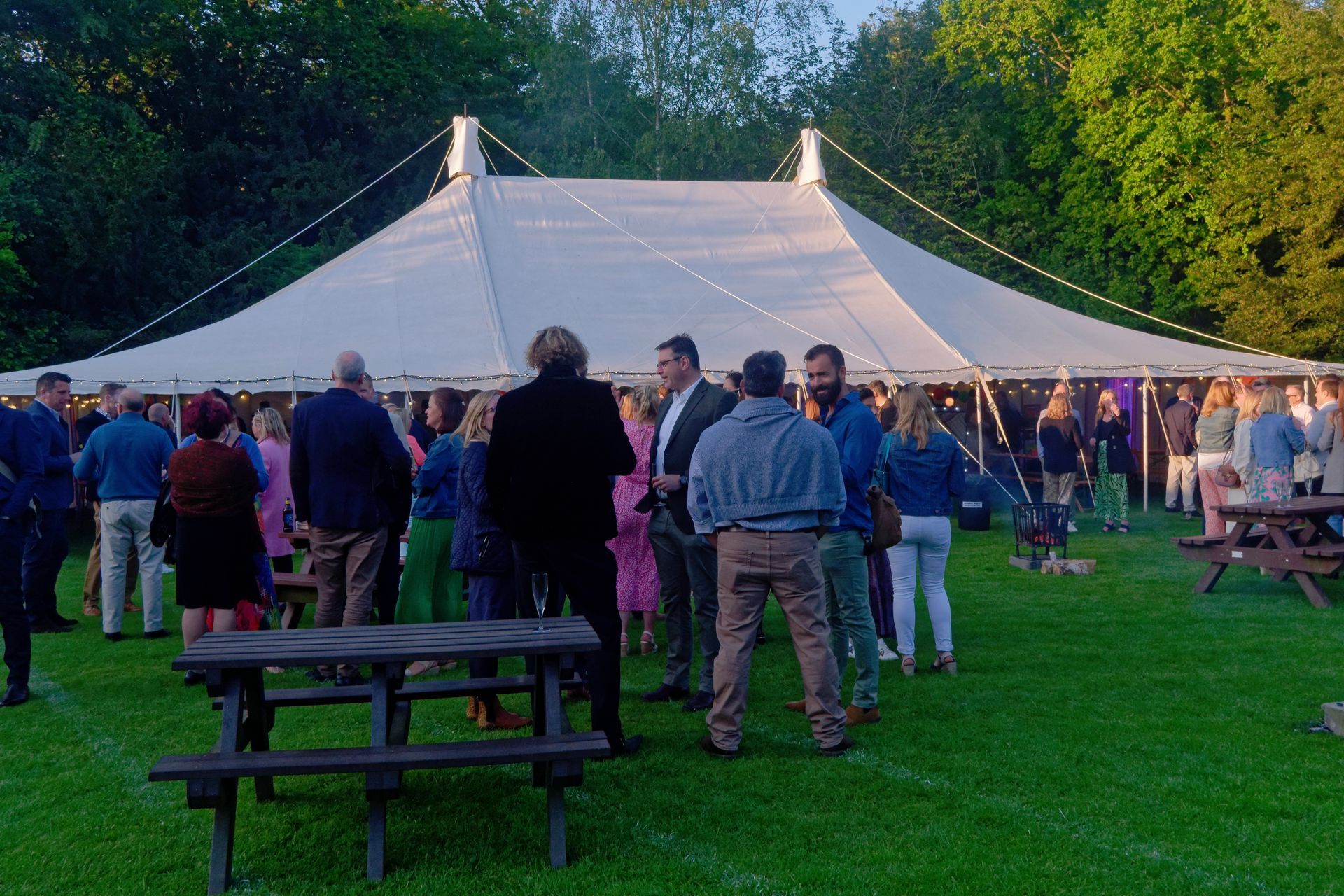 People gathered outdoors near a large white tent, enjoying a social event on a lawn.
