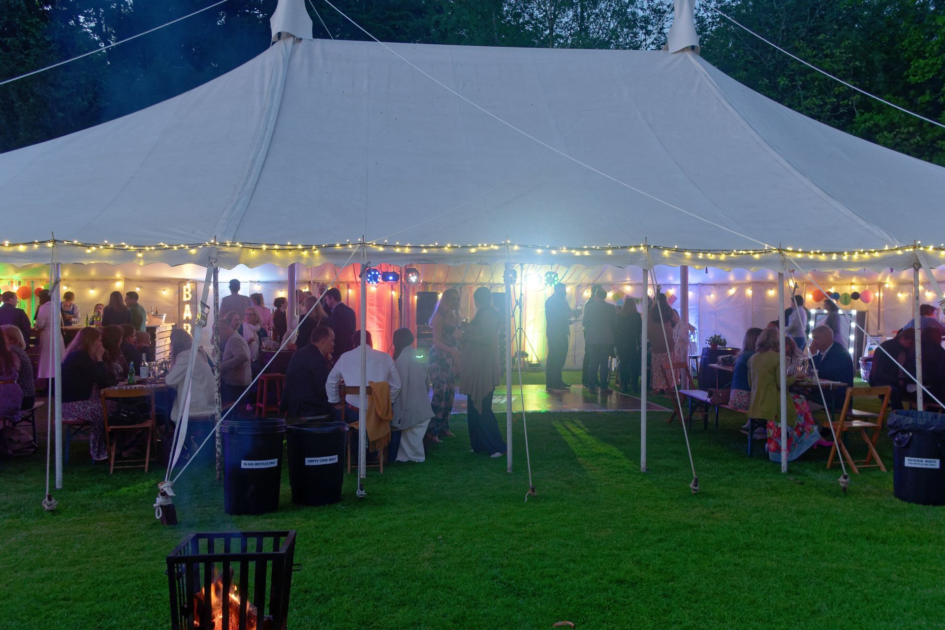 Large white tent lit with string lights, a party with people dancing and socializing on a grassy lawn.