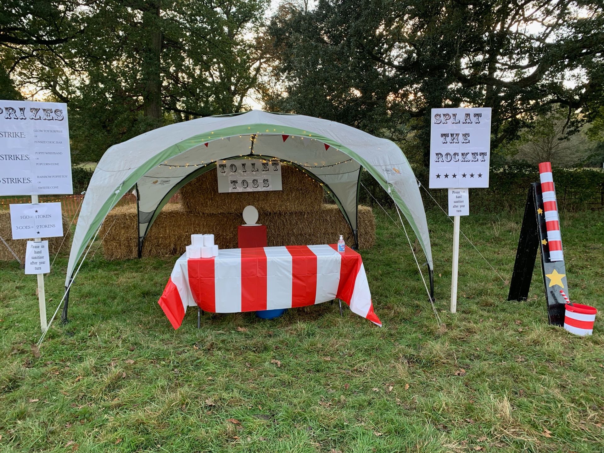 A carnival game booth in a grassy field with signs, a striped table, and a 