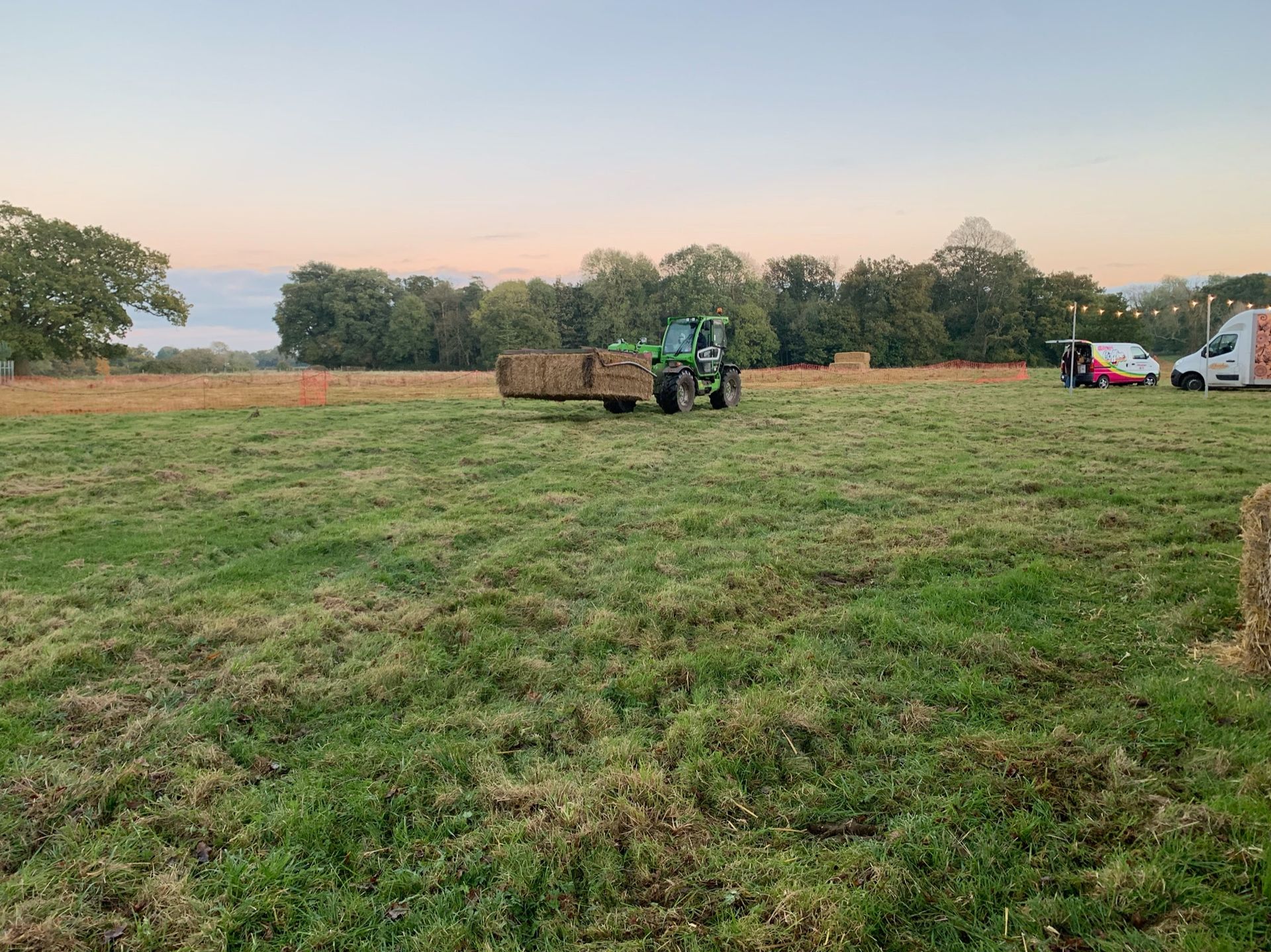 Green tractor hauling hay bales across a grassy field under a light sky.