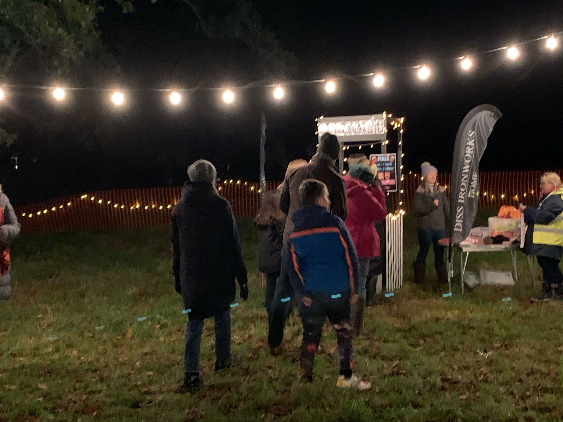 People at an outdoor nighttime event, under string lights and near a food stall.