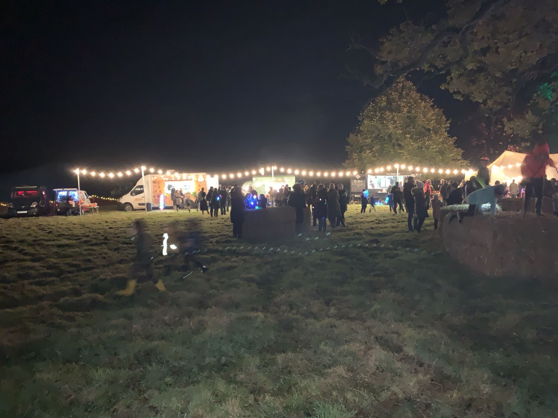 Nighttime outdoor food market with strung lights, food trucks, and people.