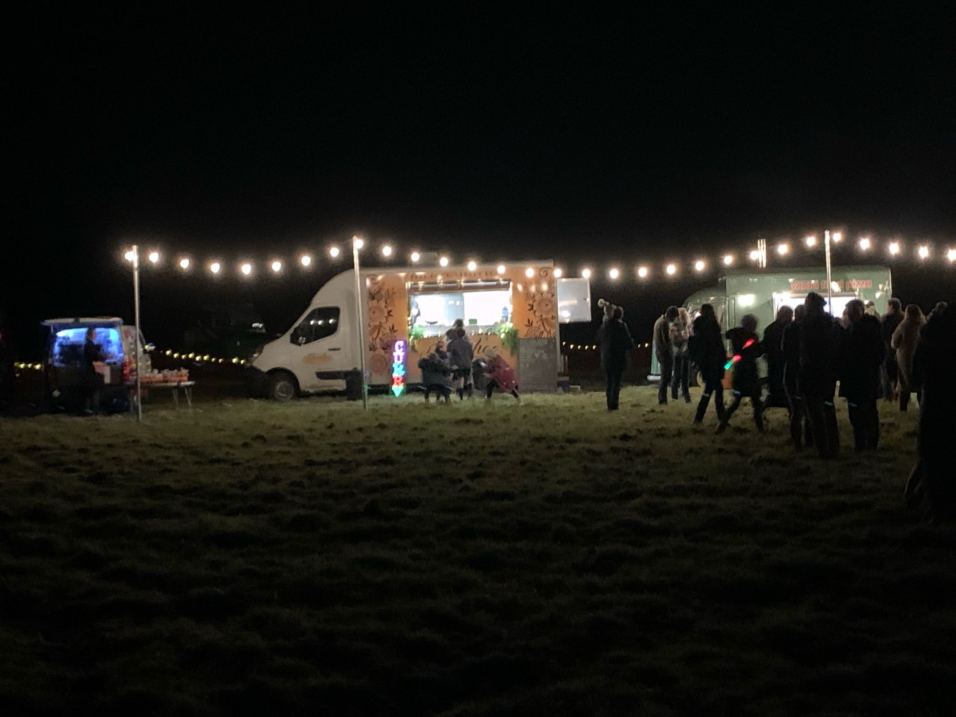 Food trucks at night, lit by string lights, people gather on grass.