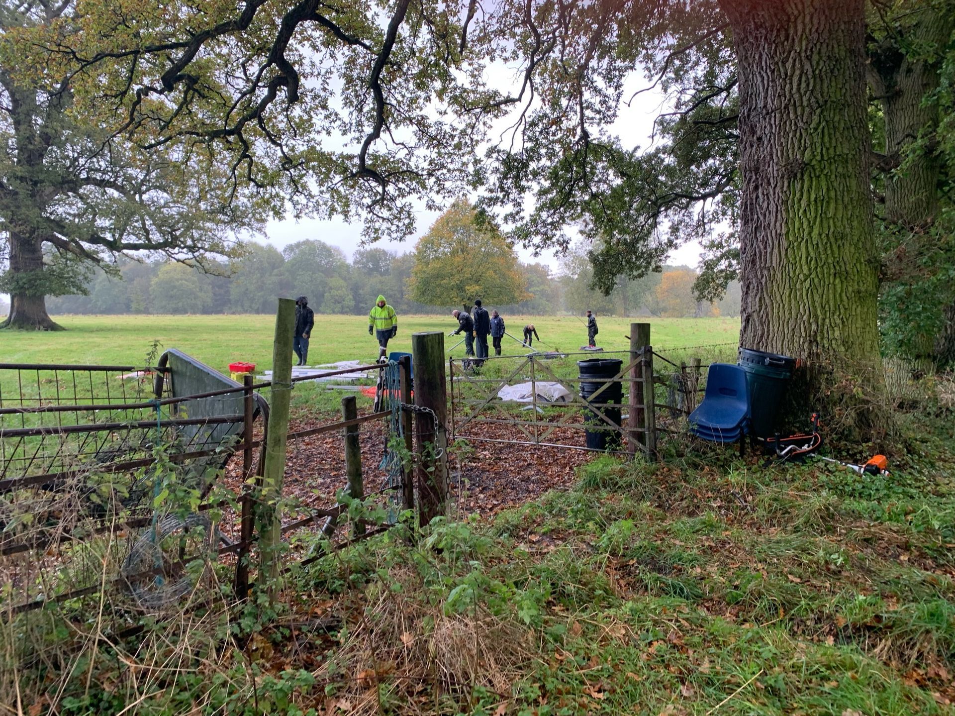 People near a gate in a field, with trees. Overcast sky.