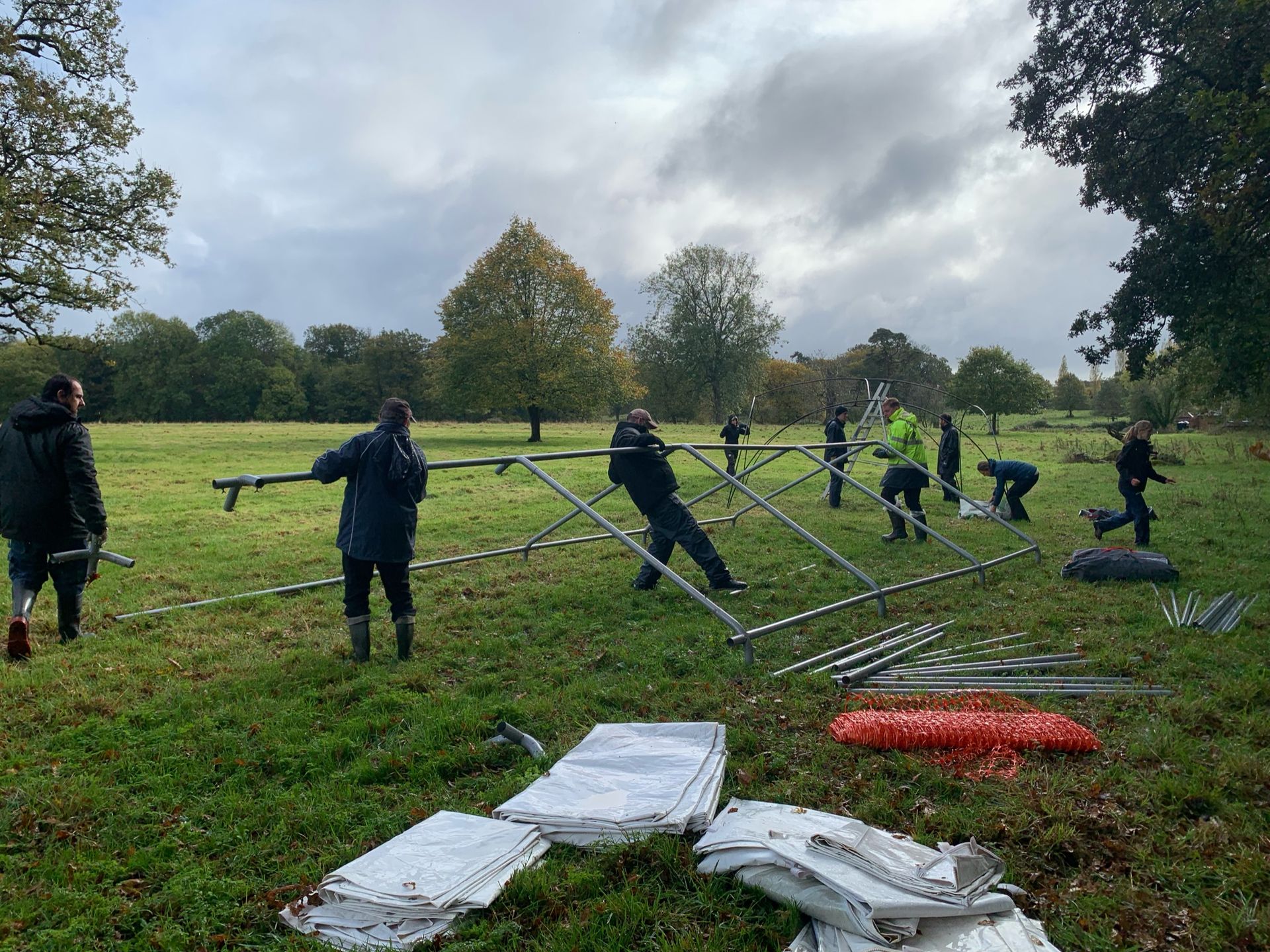 People assembling metal structure in grassy field under cloudy sky.