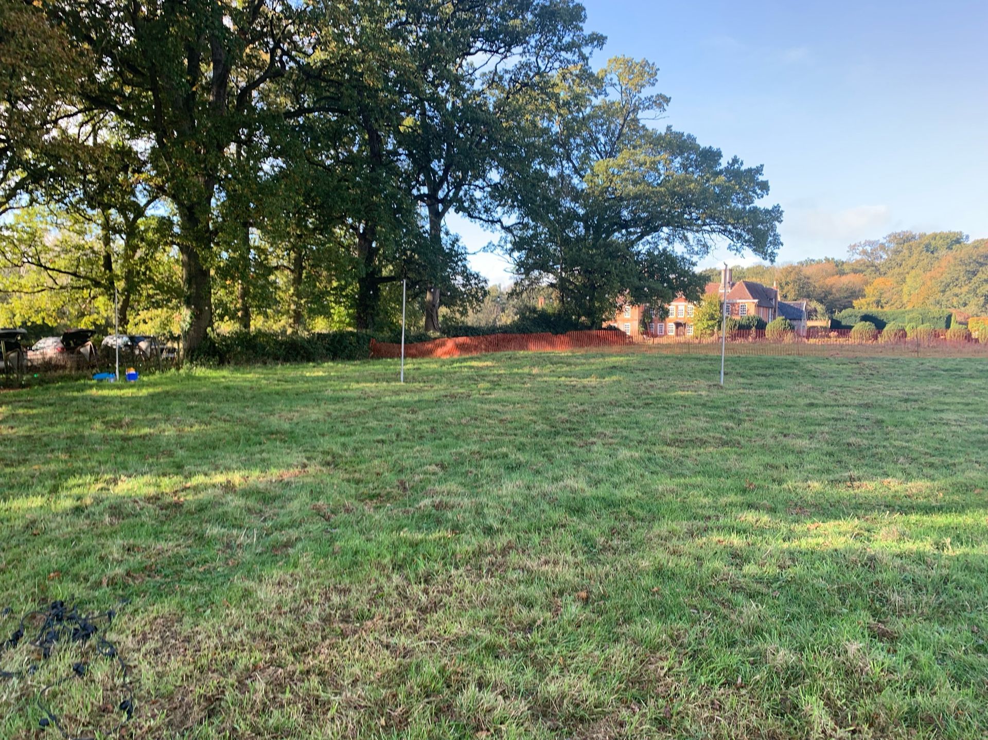 A grassy field with trees and a house in the background under a blue sky.