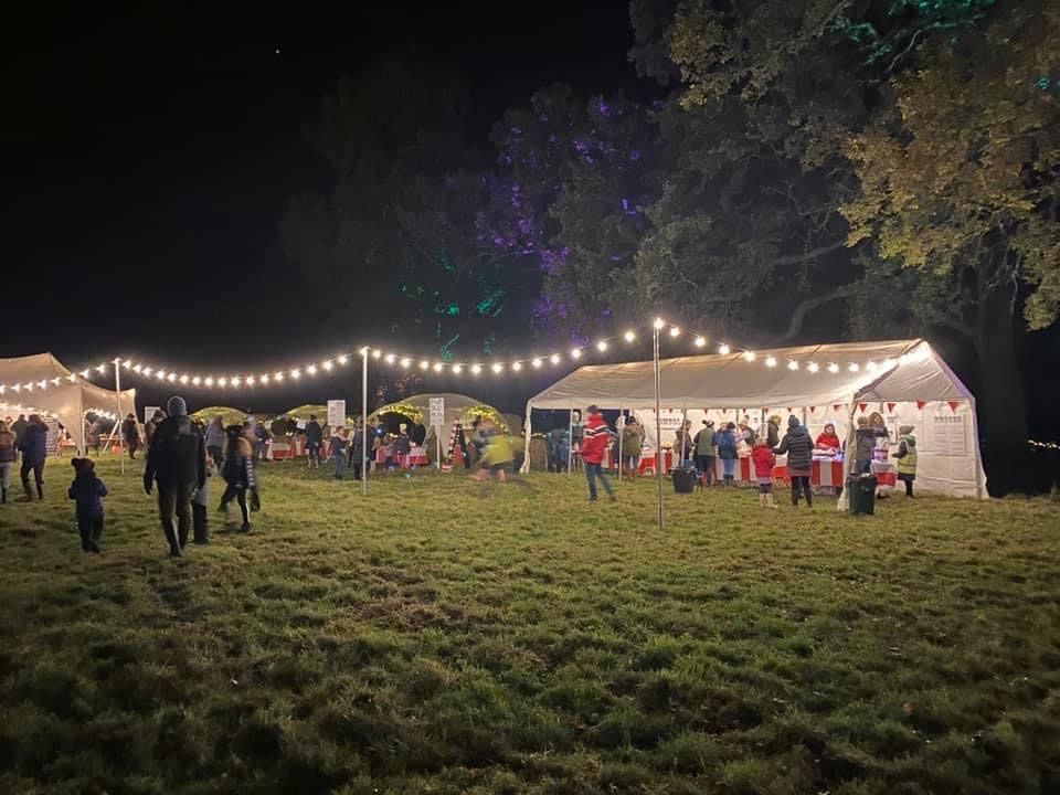 Nighttime outdoor event with tents, string lights, and people on a grassy field.