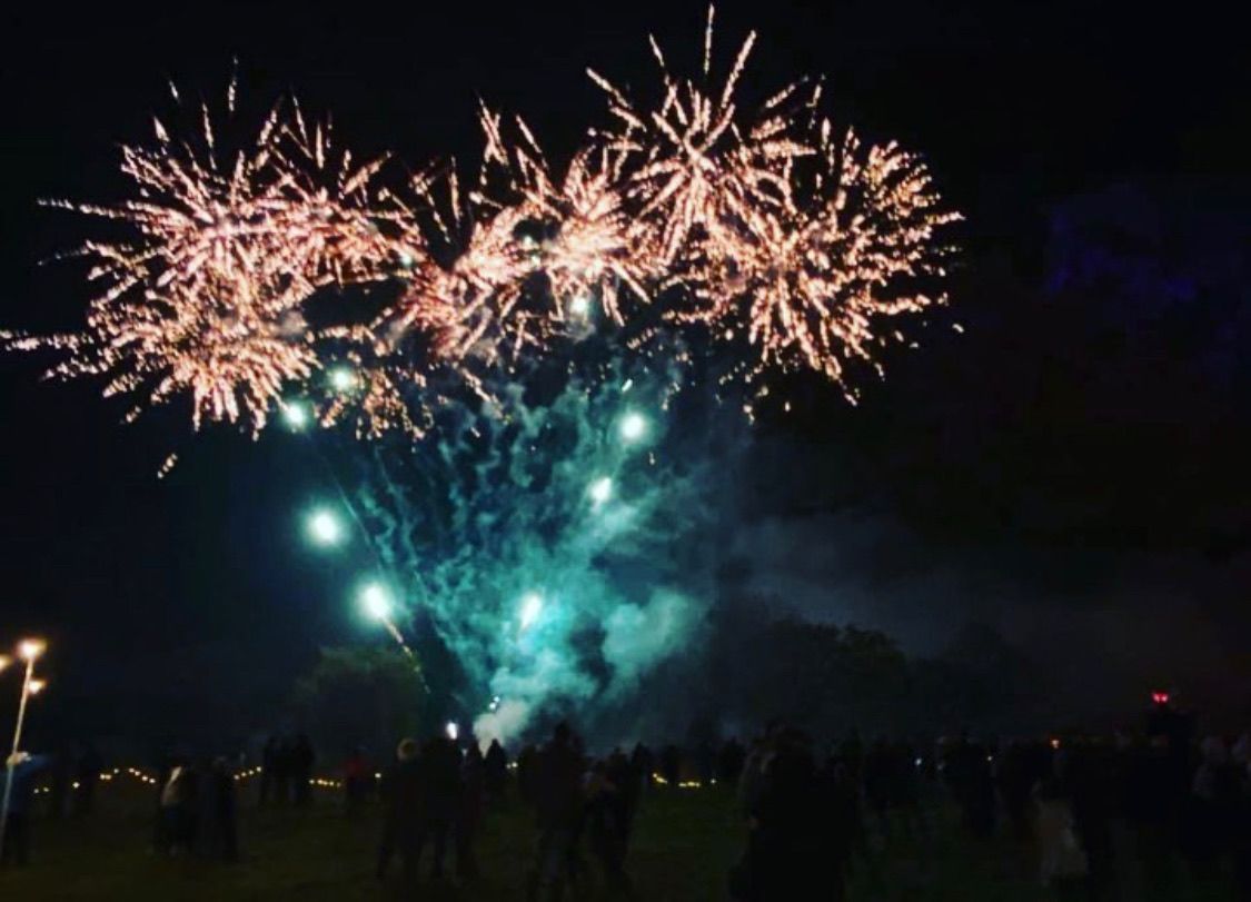 Fireworks exploding over a crowd at night. Bright colorful bursts with teal and gold hues.