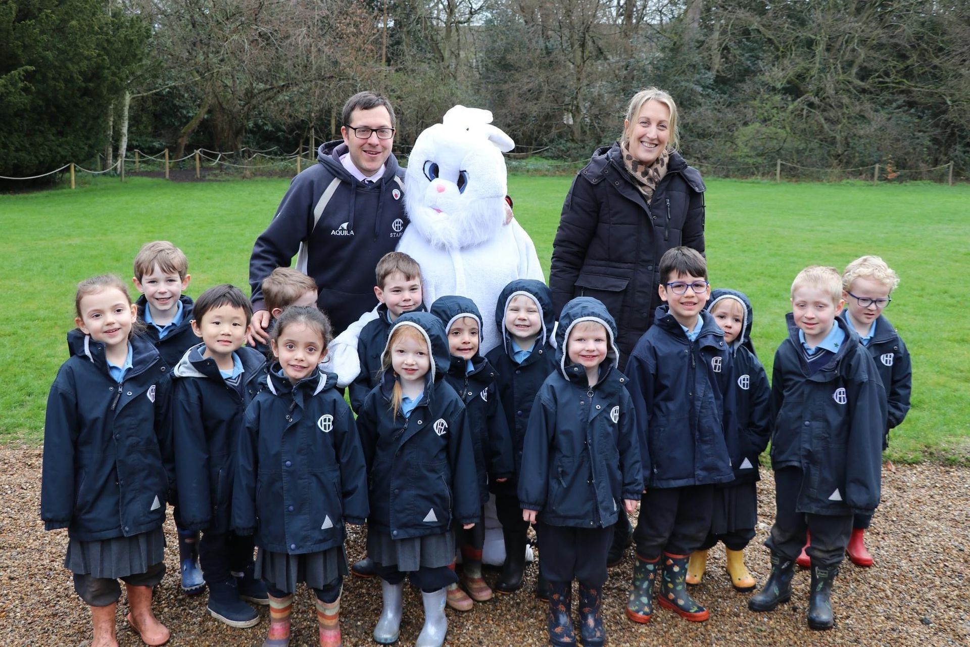 Group photo: Children with adults and a white bunny mascot outdoors.
