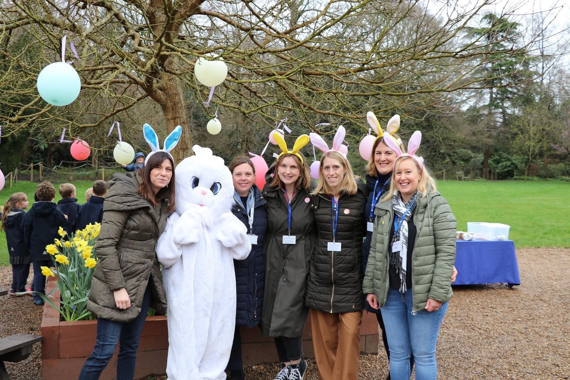 Group of people with bunny ears, a person in a bunny costume, and Easter decorations outdoors.