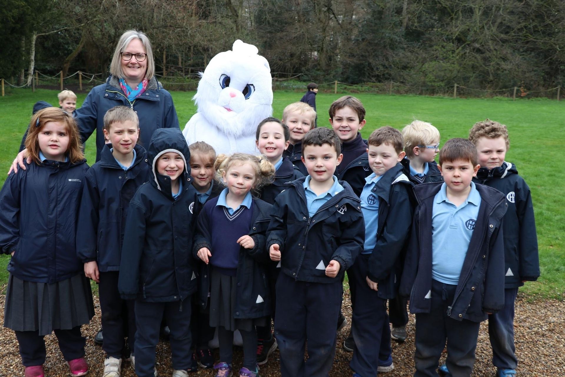 Group of schoolchildren with a person and a bunny mascot in a park, all smiling.