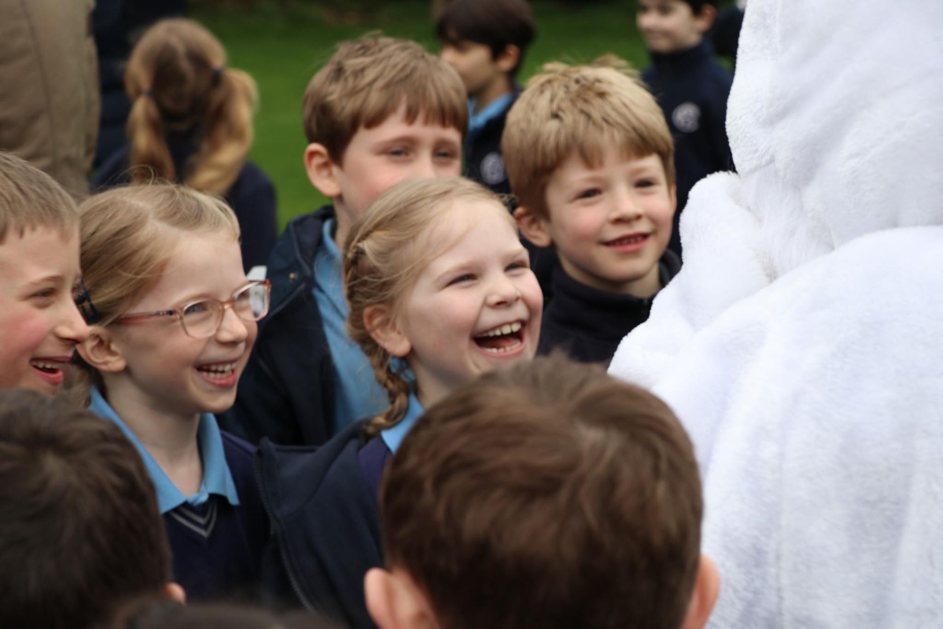 Children in school uniforms laugh while interacting with a person in a white costume.