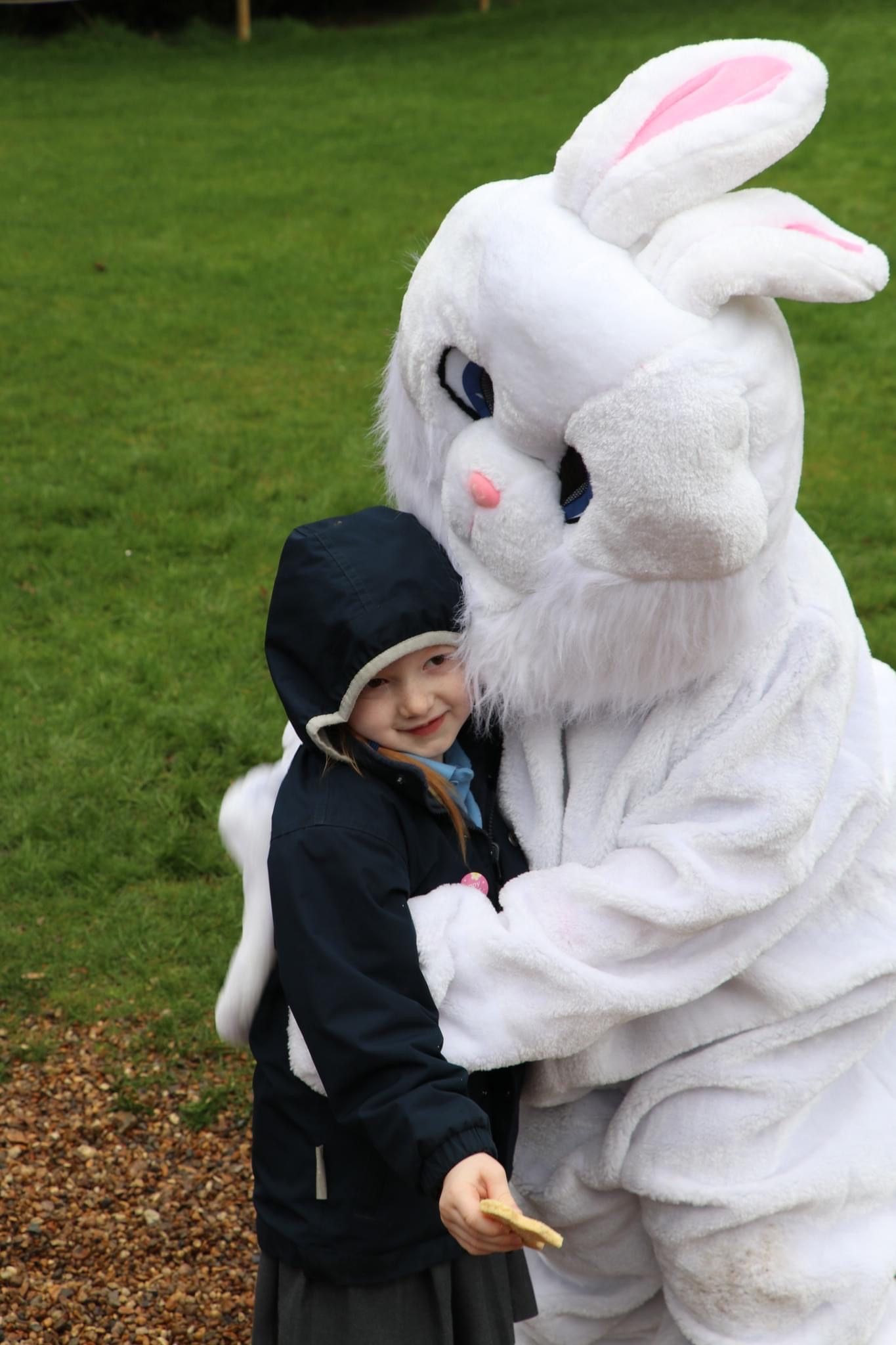 Girl in a dark jacket hugs a giant white Easter Bunny outdoors.