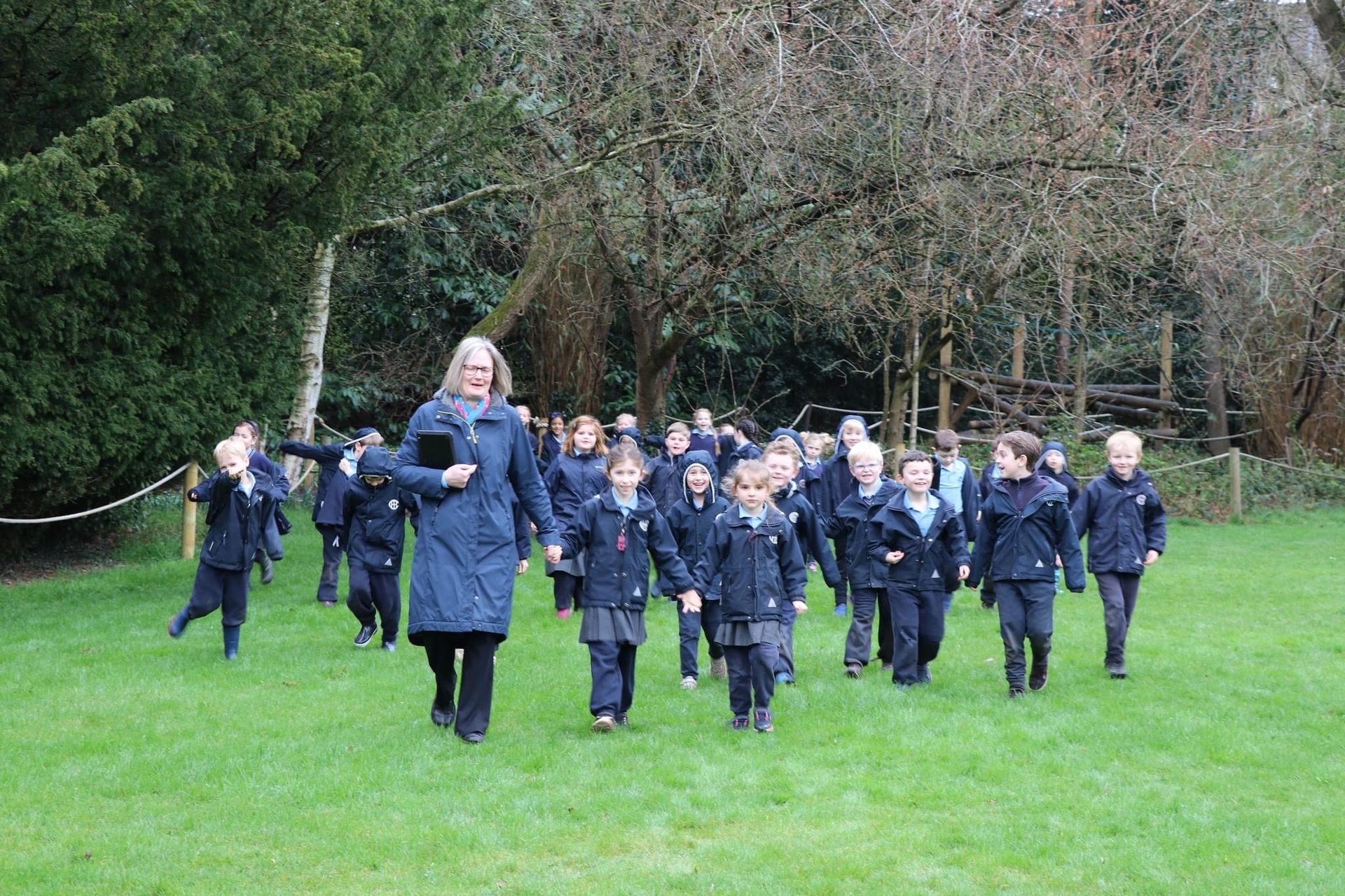 A group of students and teacher walk on green grass. They are in dark blue school uniforms.