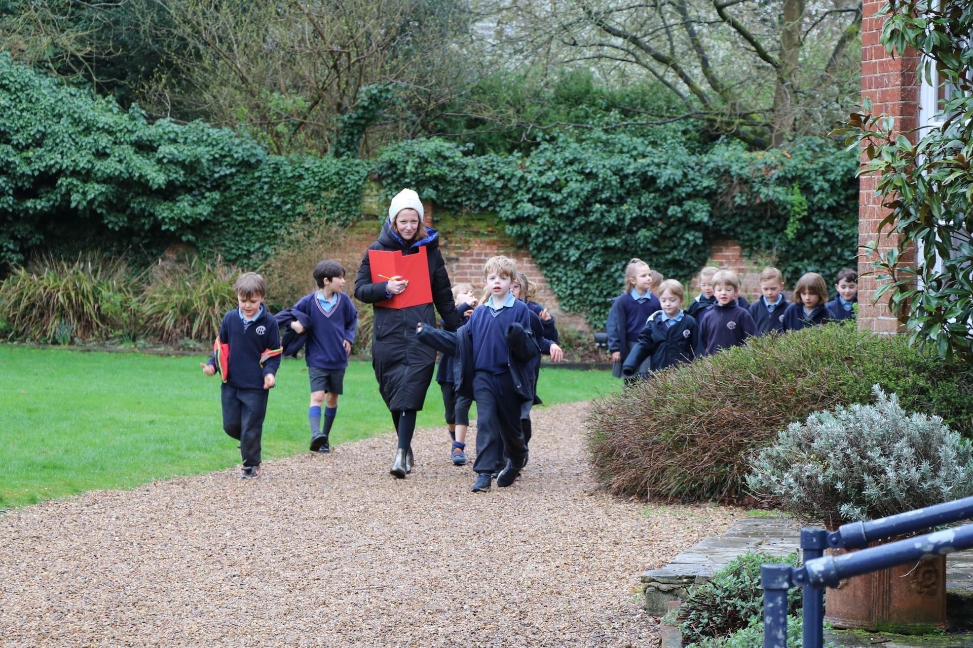 A group of school children in uniform running with a teacher on a stone path towards a building.
