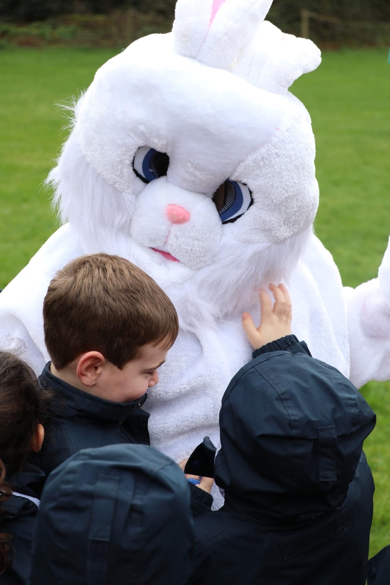 Children interacting with a person in a white Easter Bunny costume outdoors.