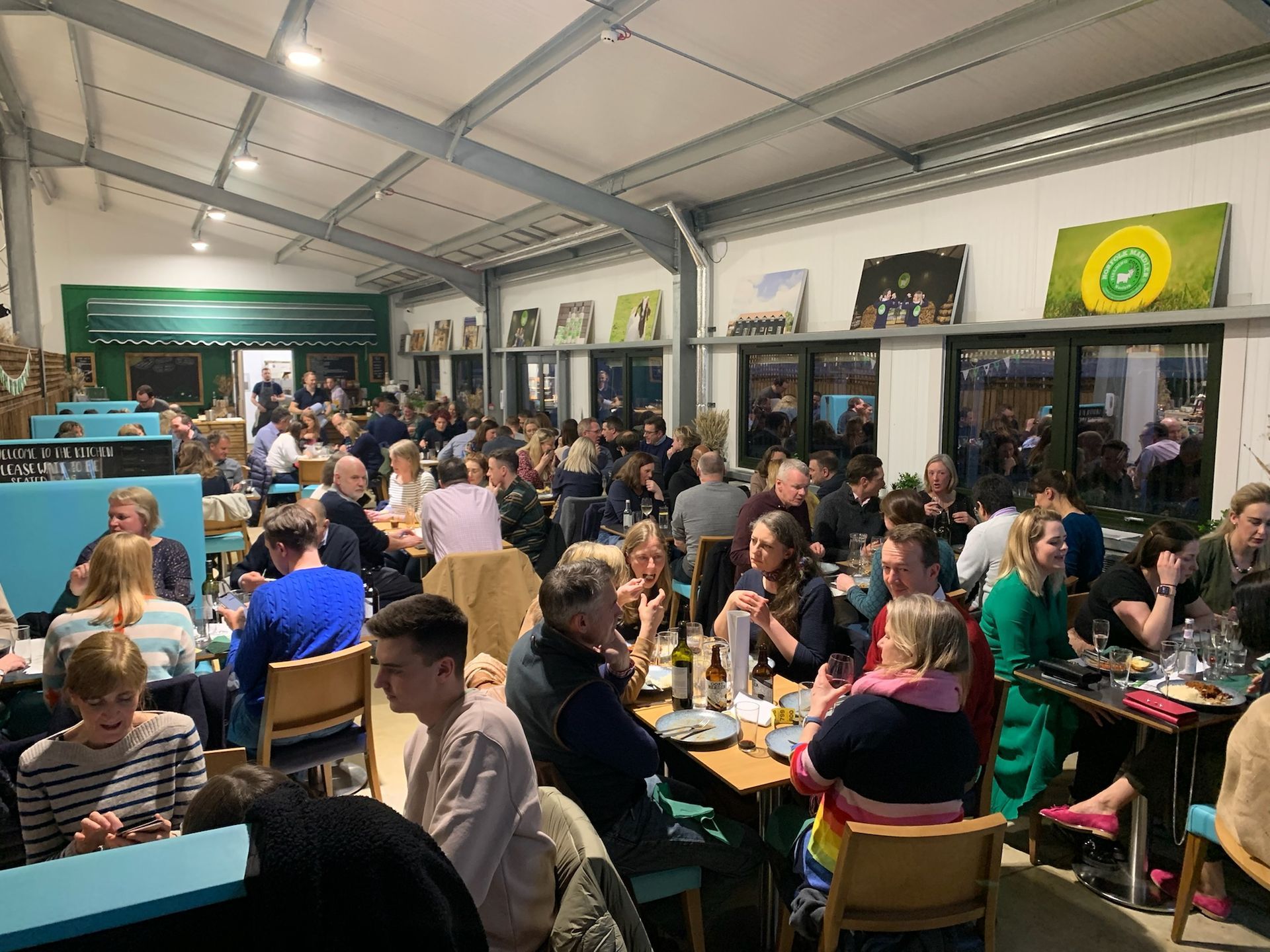 Restaurant interior filled with people eating and talking. Tables, chairs, and art on the walls.
