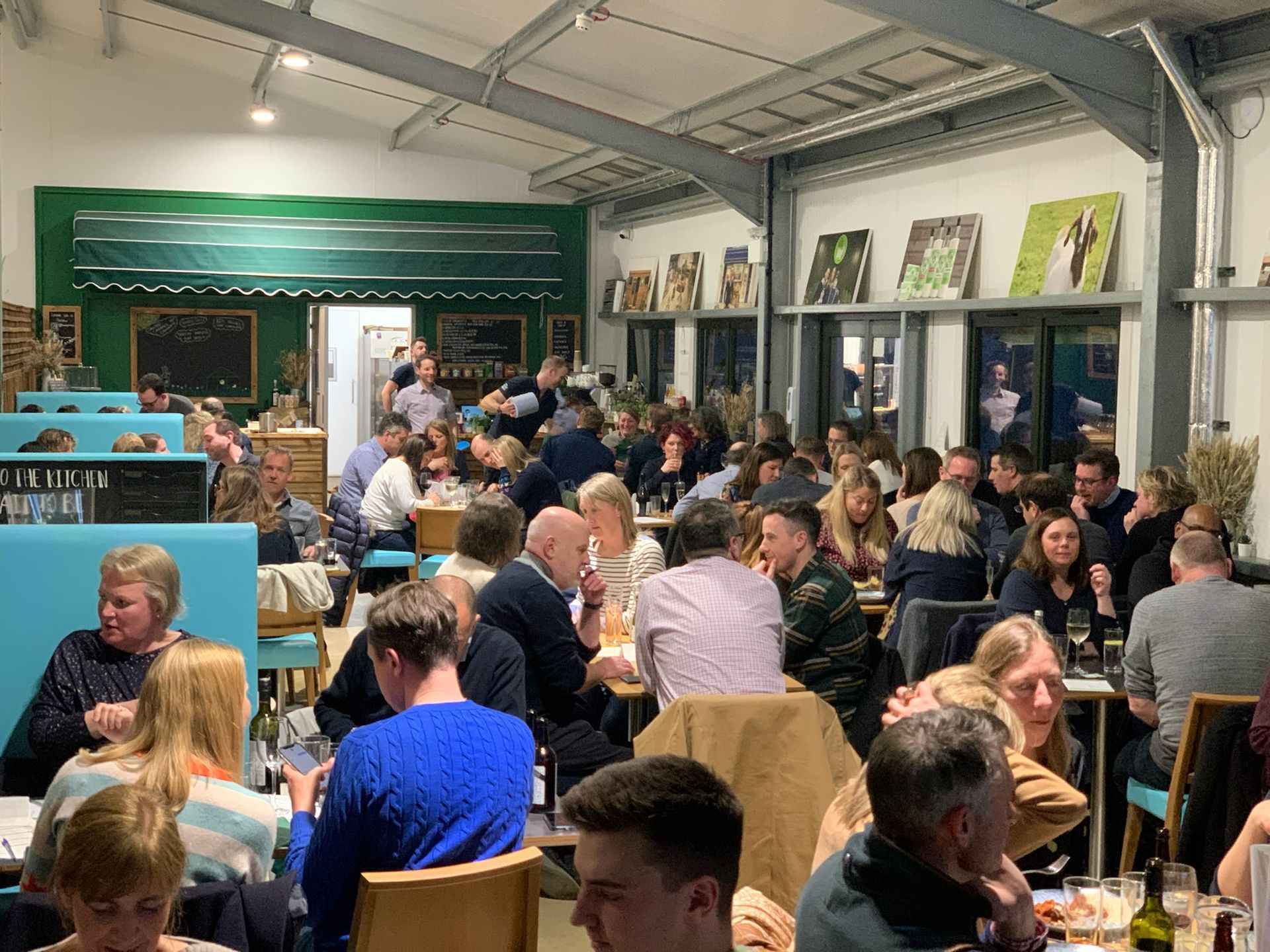 Restaurant interior; large group of people dining at tables. Green, white, and blue color scheme.