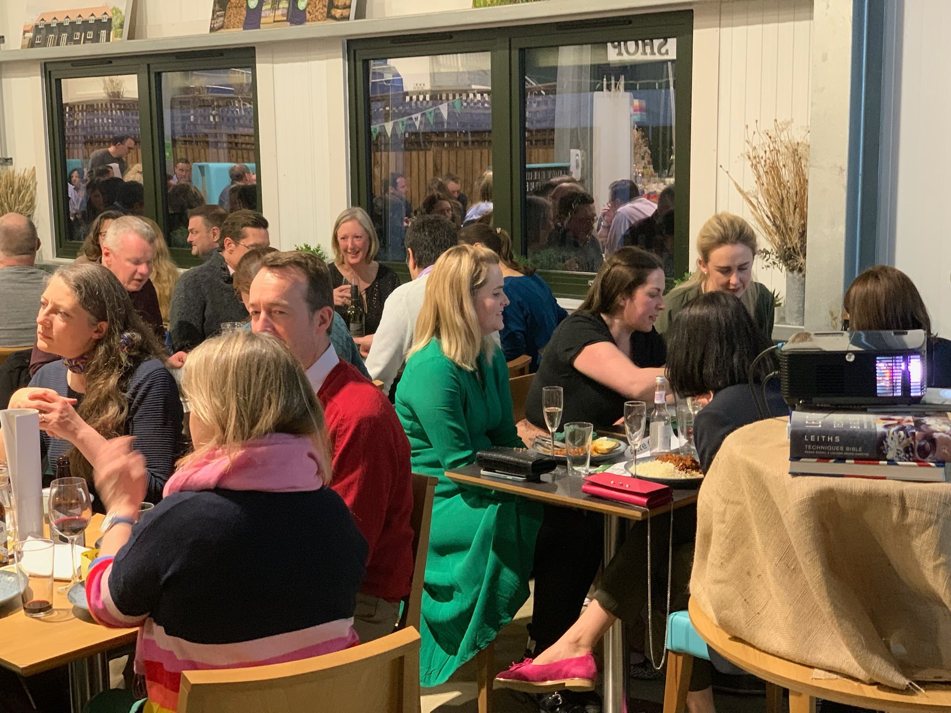 People dining inside a restaurant; diverse crowd, seated at tables, enjoying food and drinks.