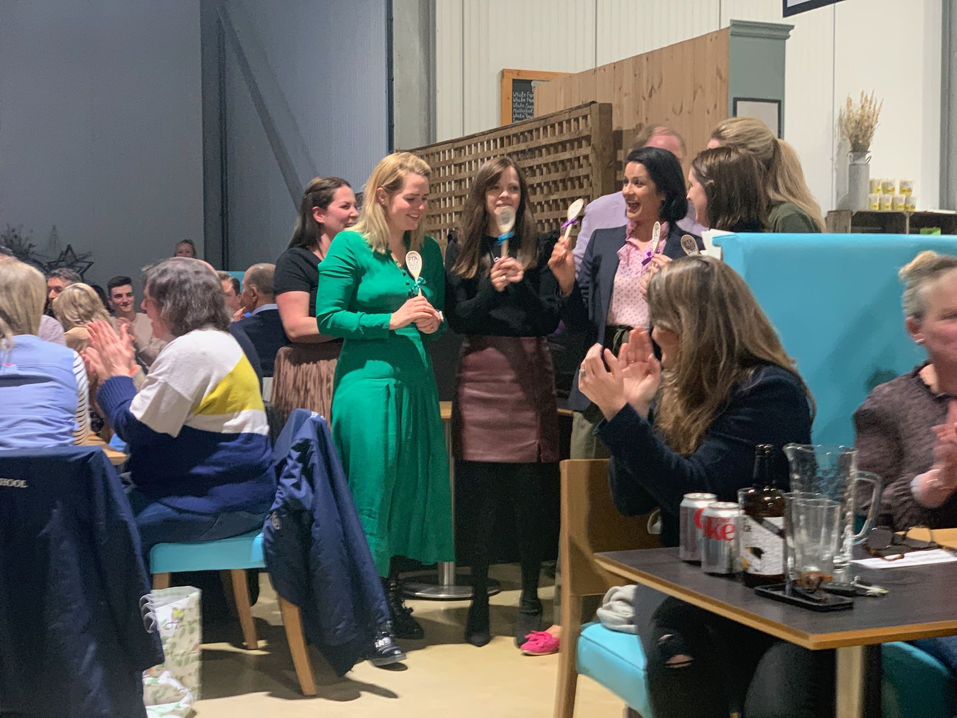 People in a room clapping, celebrating. Several women in the center hold glasses and speak.