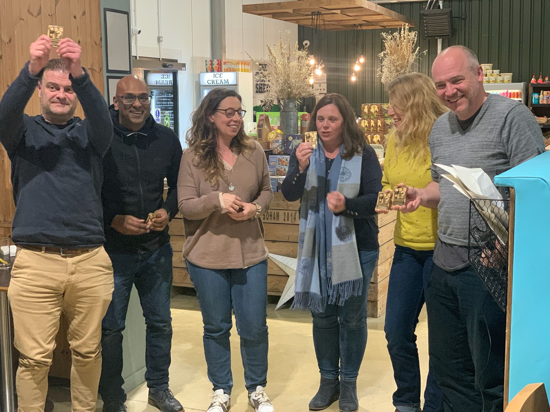 Six people celebrating indoors with food, some smiling and holding items up.