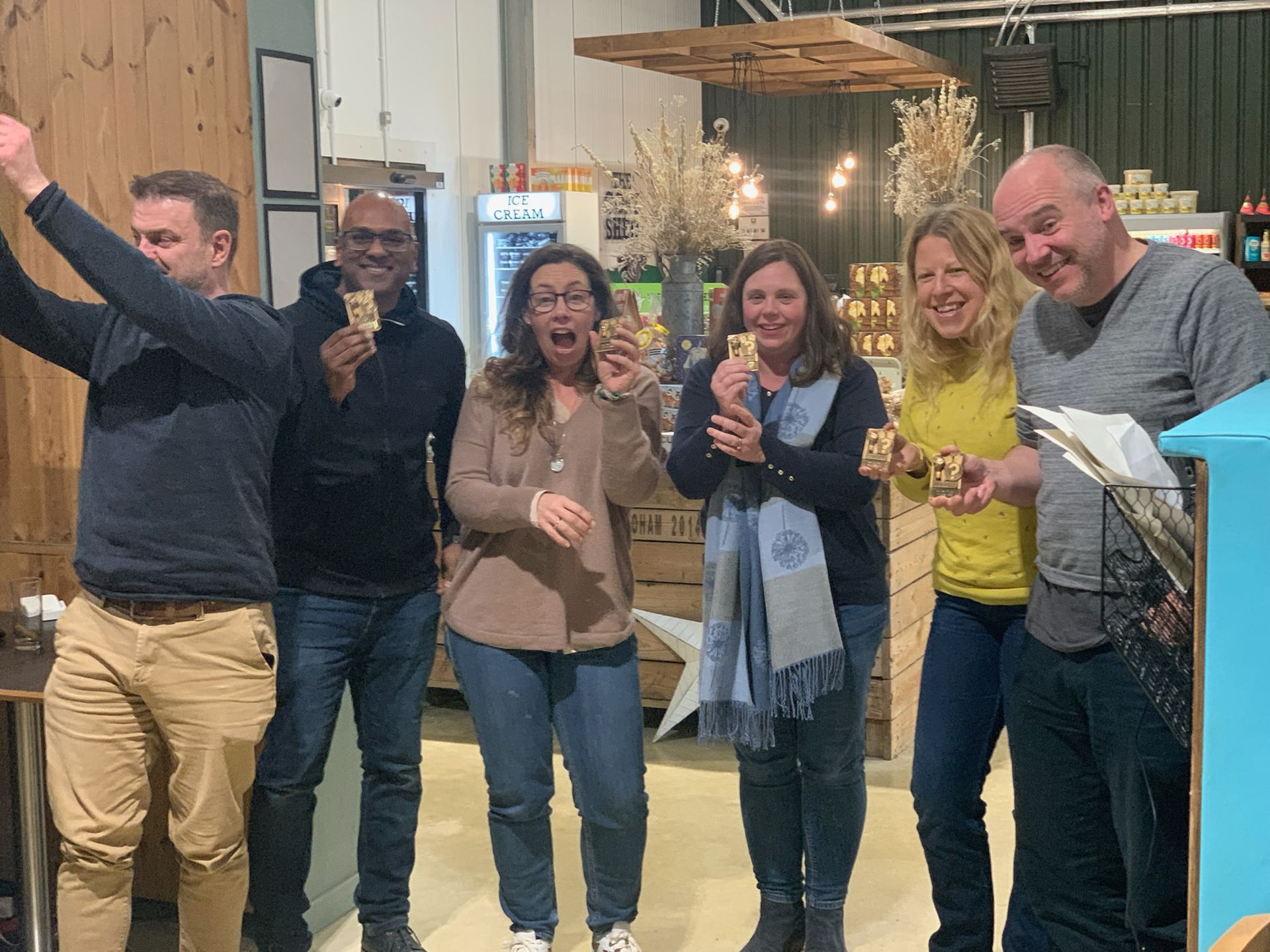 Group of people tasting food, some with surprised/happy expressions, indoors by a counter, and lights.