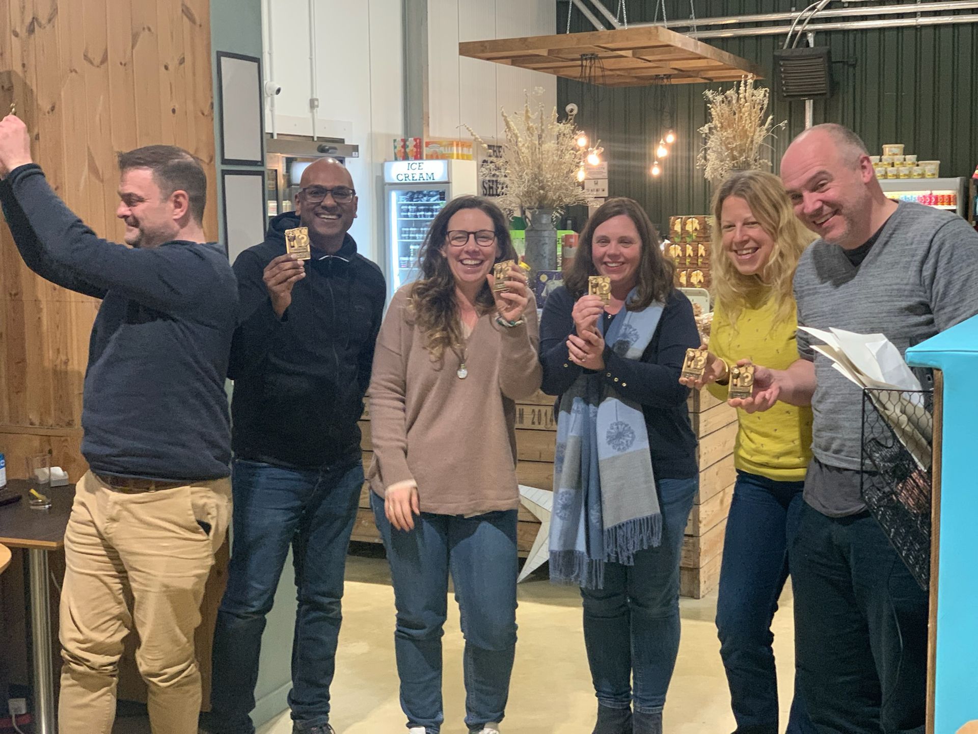 Group of six people holding up small items, smiling, indoors.