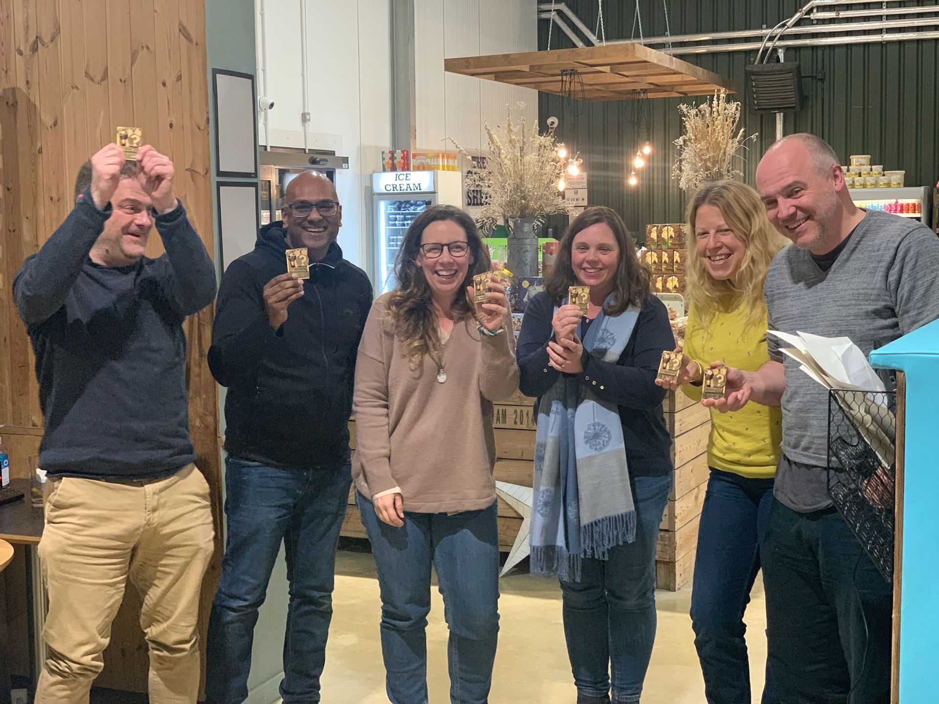Six people holding up food items, smiling, in a shop setting.