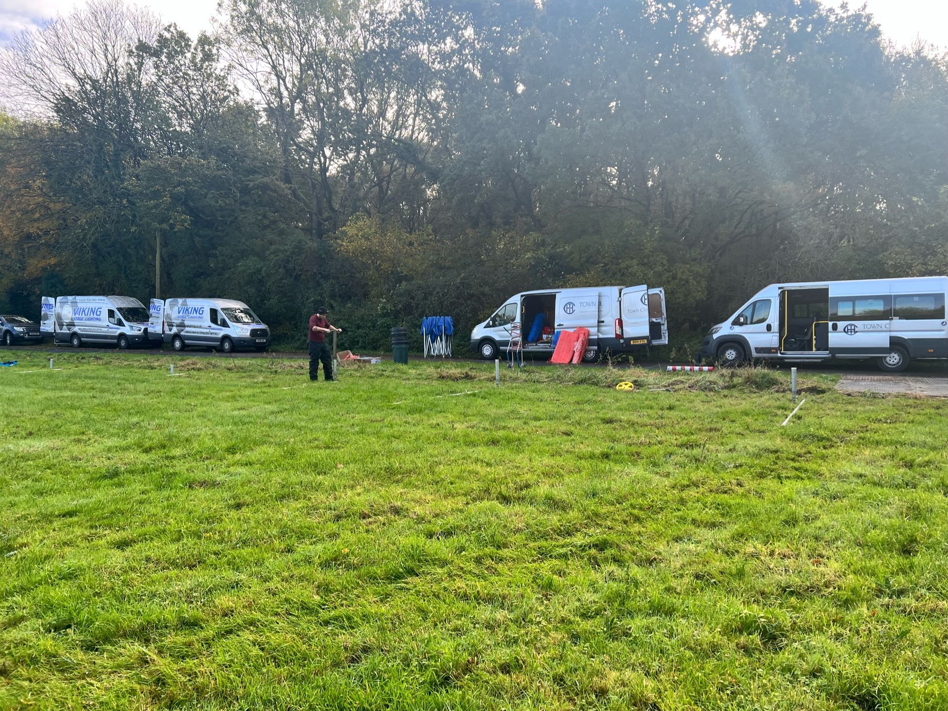 Vans parked in a grassy field with a person standing nearby, trees in the background.