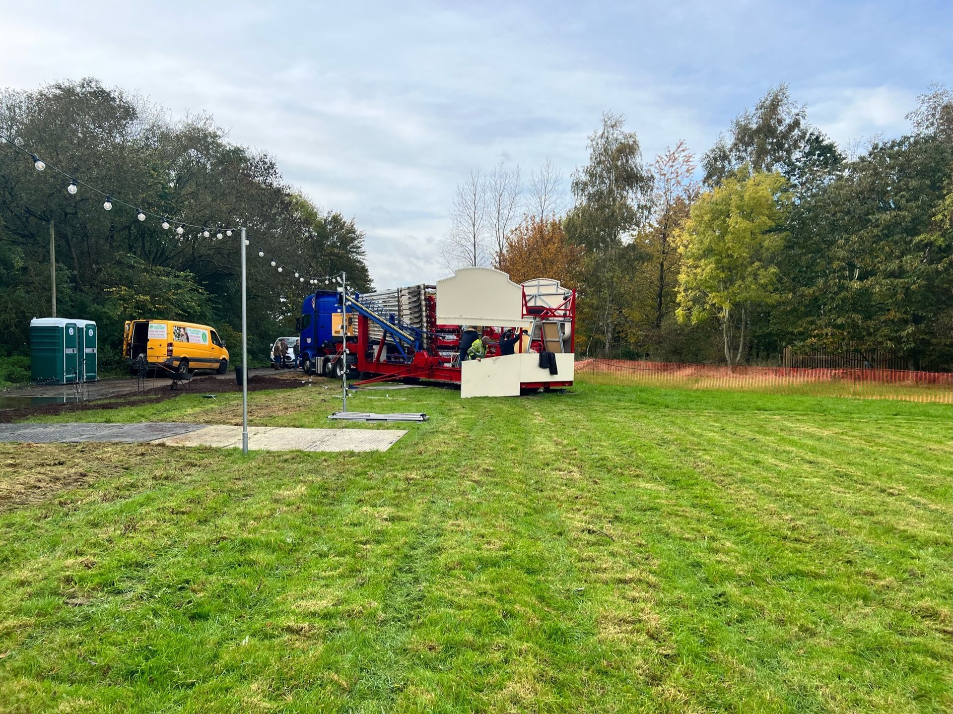 A grassy field with a carnival ride being set up, portable toilets, and trees.