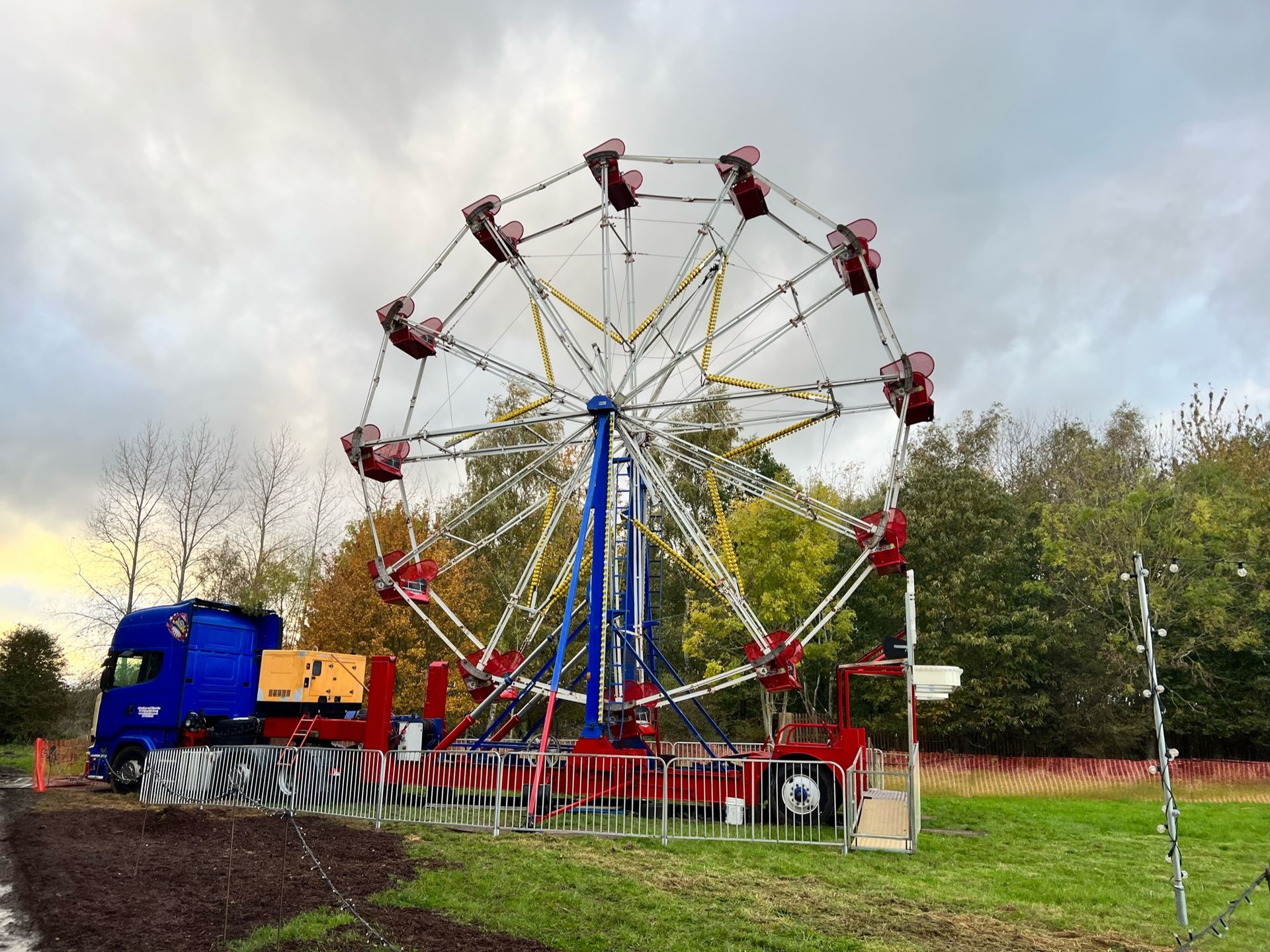 A small amusement park ride, a Ferris wheel-type ride, is parked on a grassy field with a blue truck attached.