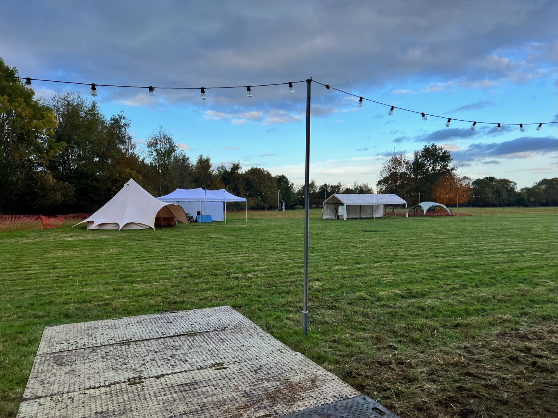 A grassy field with tents, string lights, and a cloudy sky.