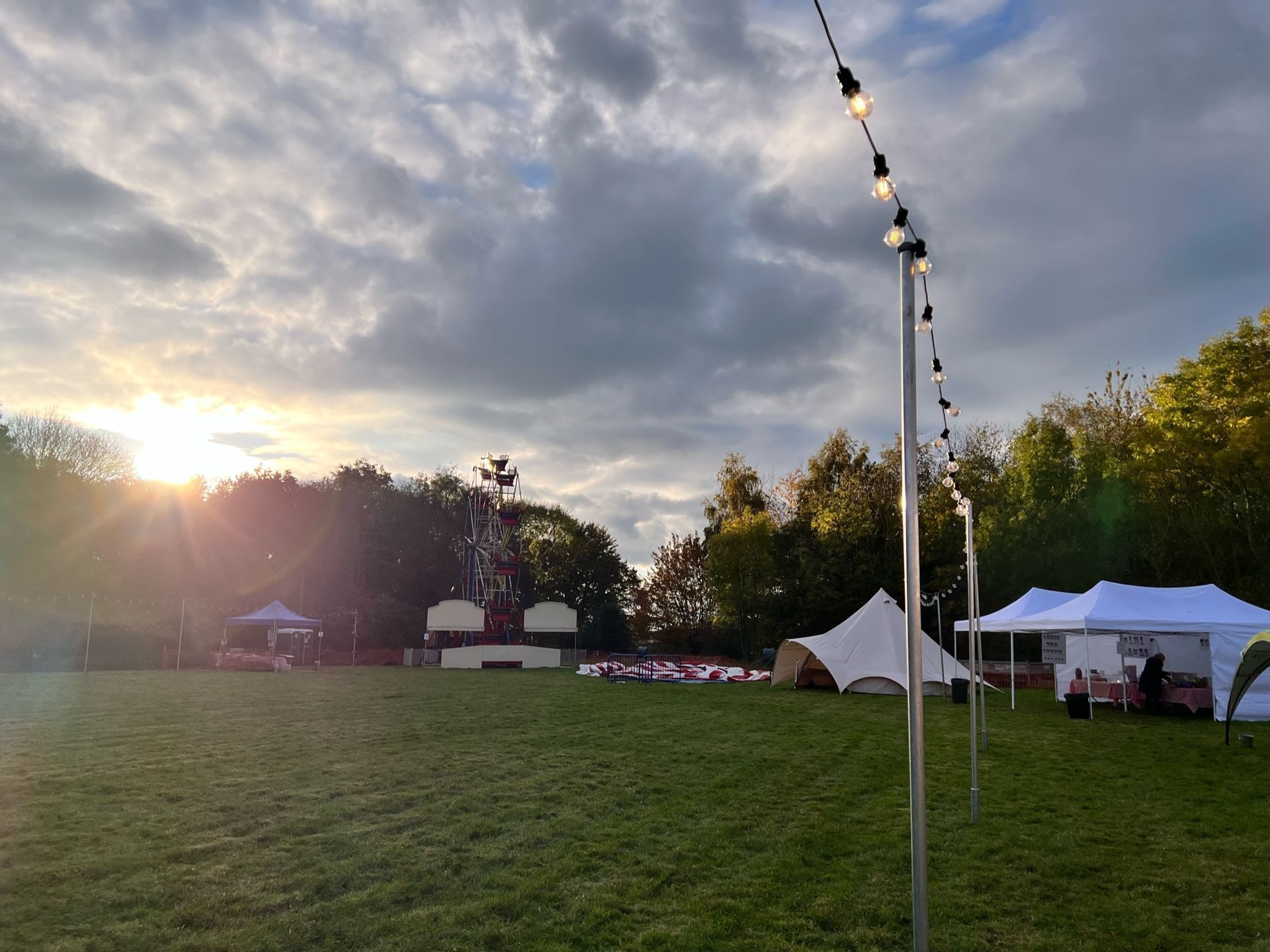 Outdoor event with tents, string lights, and trees; sunset casting light on the grass field.