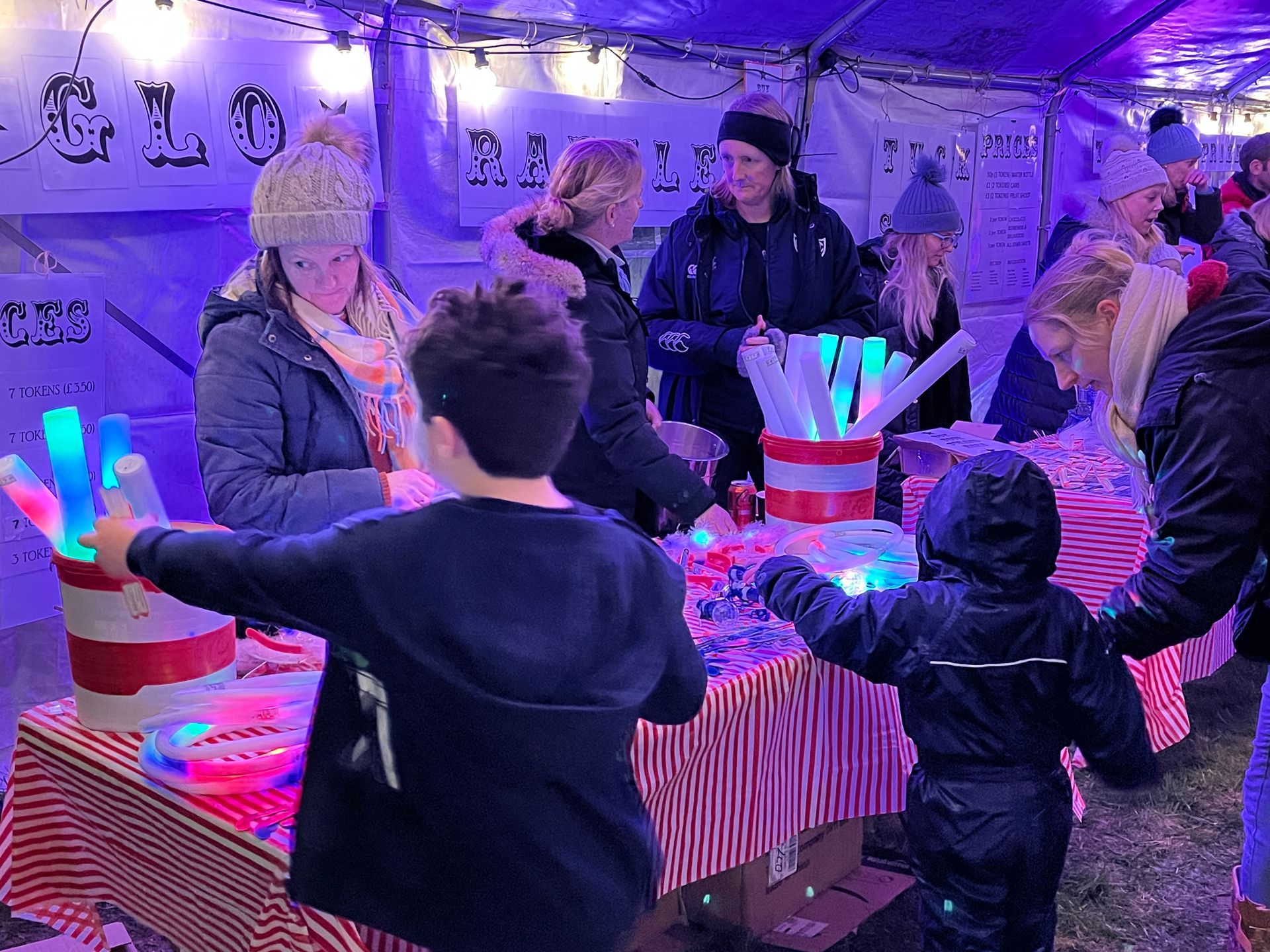 Children with glowing toys at a festive outdoor market stall, lit with purple lights.