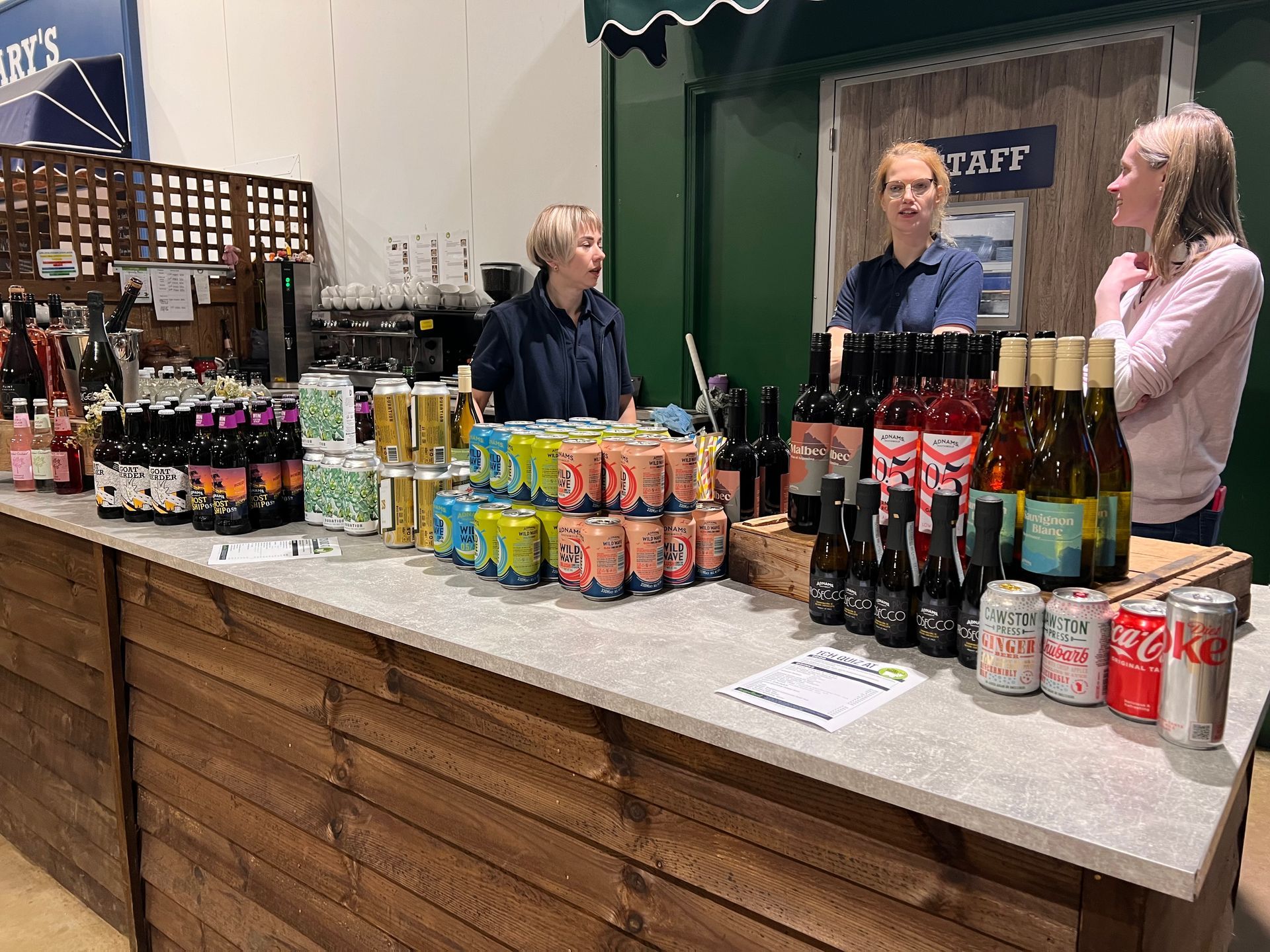 People at a bar selling drinks. A variety of colorful cans and bottles are displayed on the counter.