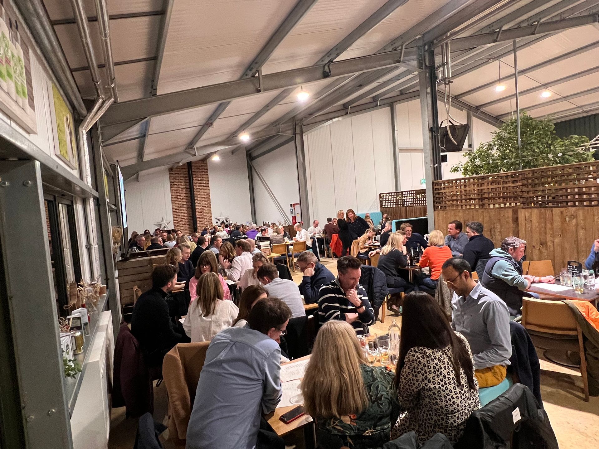 Large event in a brightly lit industrial-style building with many people socializing at tables.