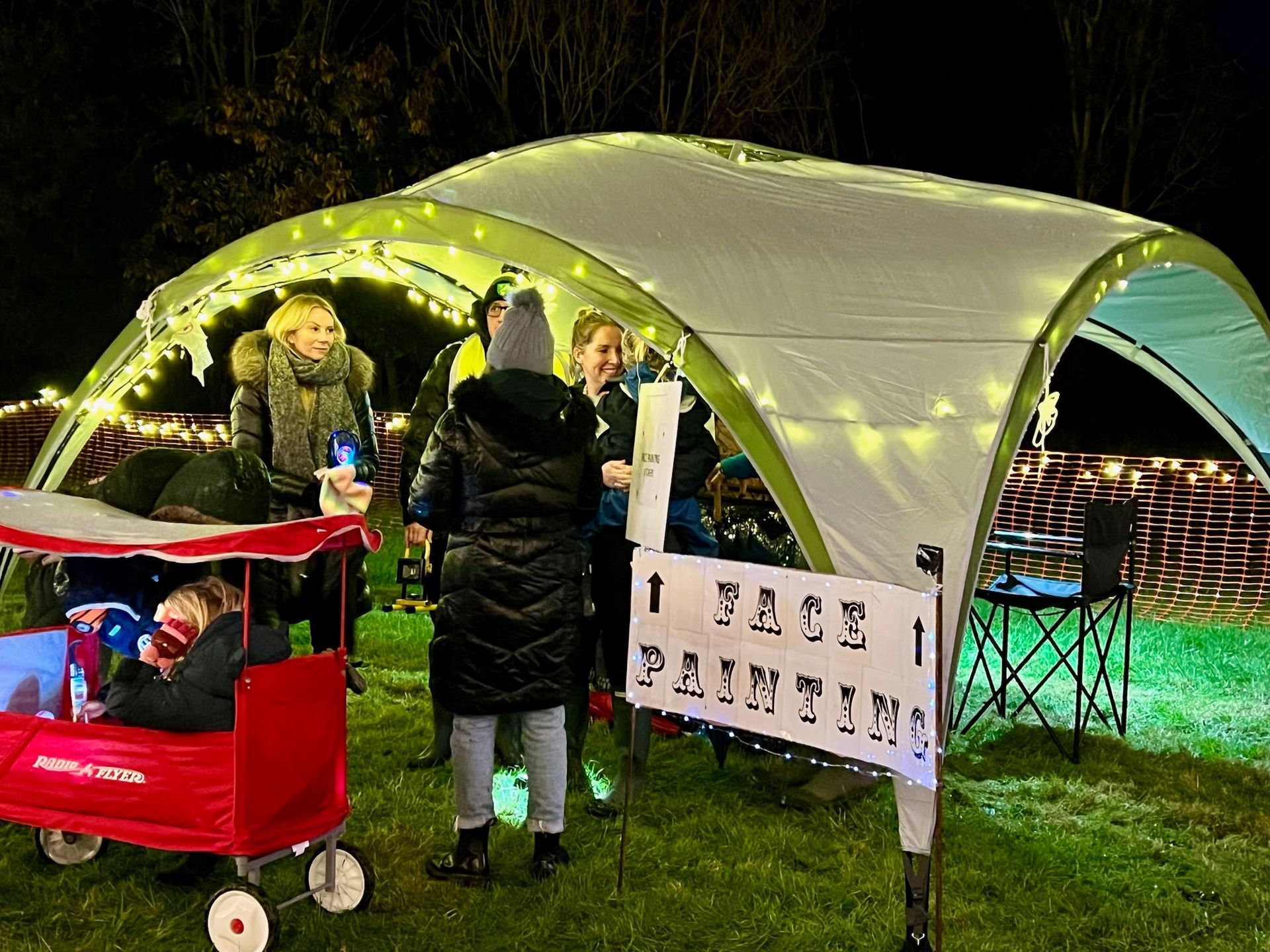 People at a nighttime event. A tent with fairy lights has a 