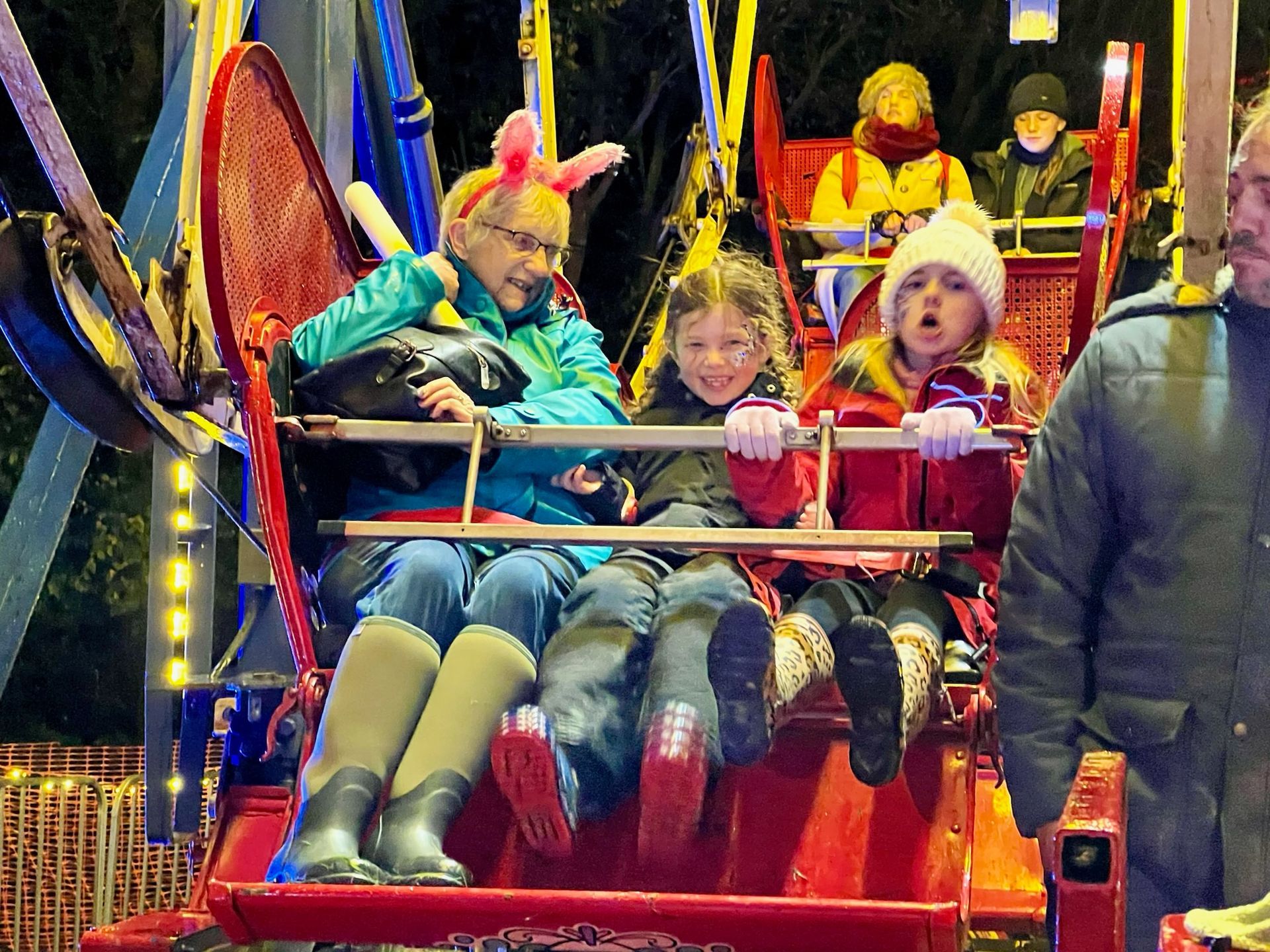 People riding a red amusement park swing ride at night, smiling.
