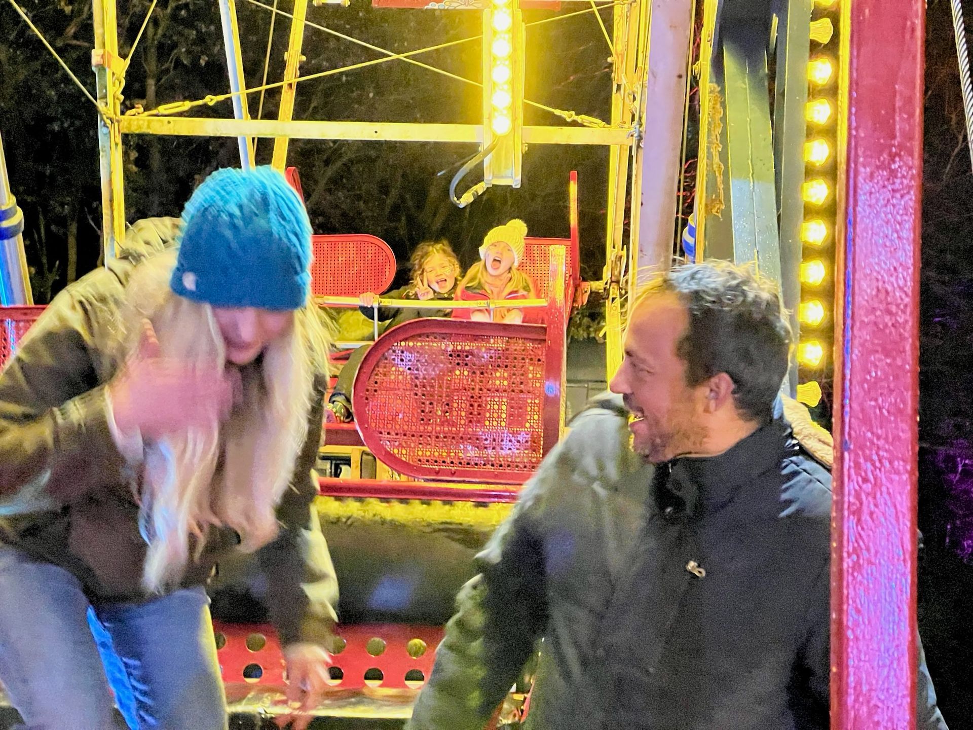 People exiting a carnival ride at night. A woman and man react, smiling, while children are in the ride behind them.