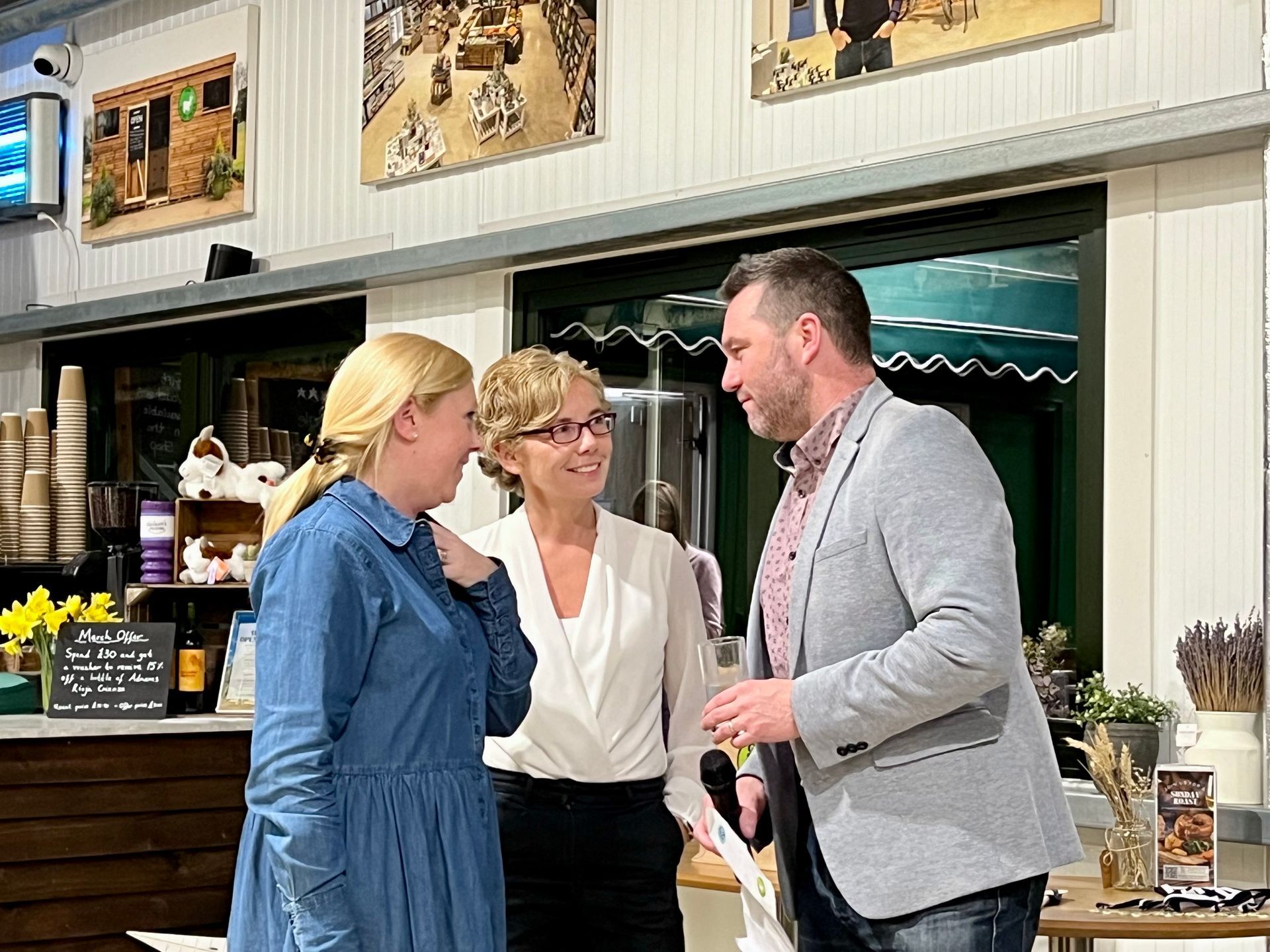 Three people talking in a cafe, two women and a man holding a microphone.