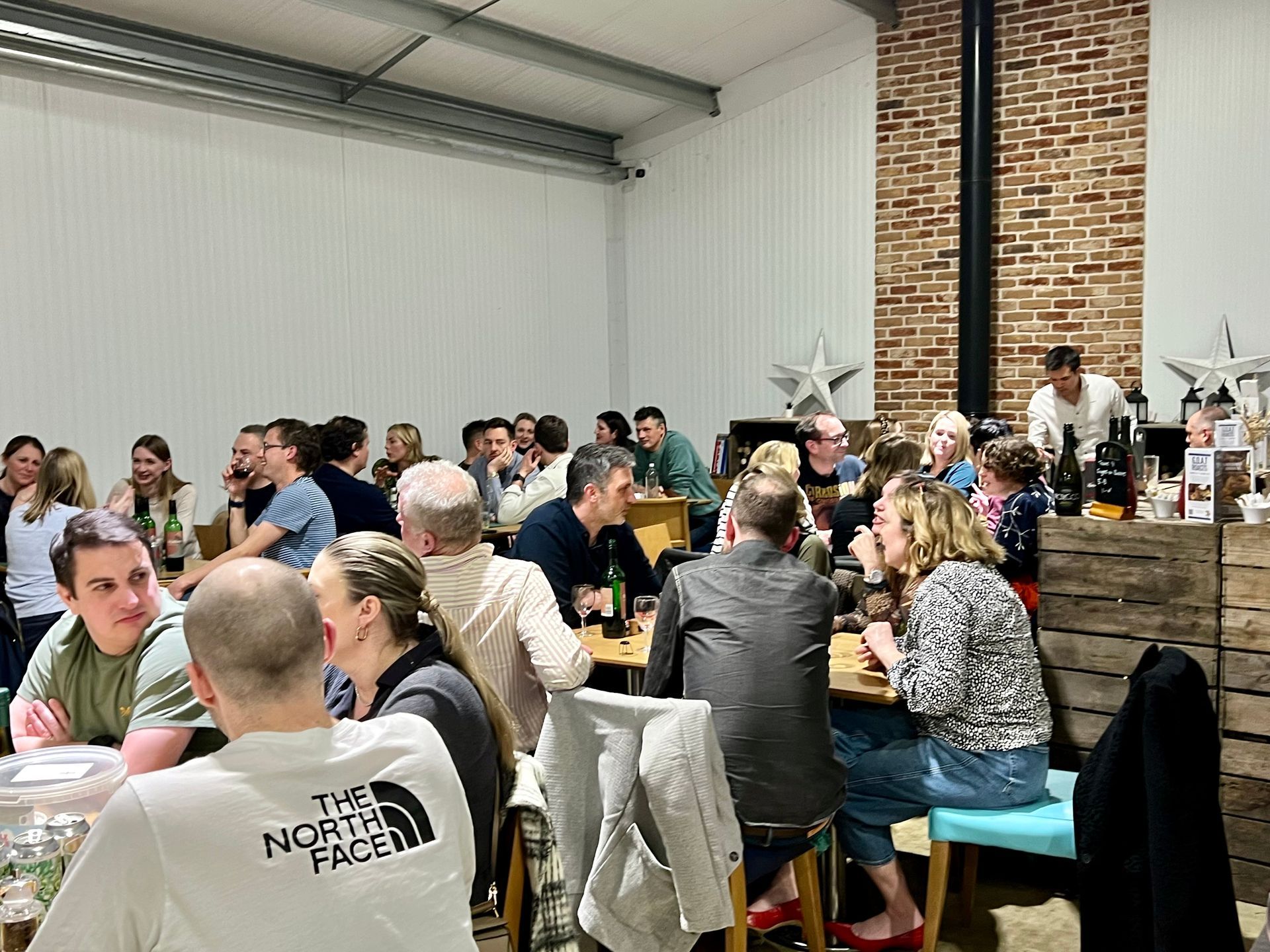 People seated at tables in a large room with a brick pillar. Several people are talking and smiling.
