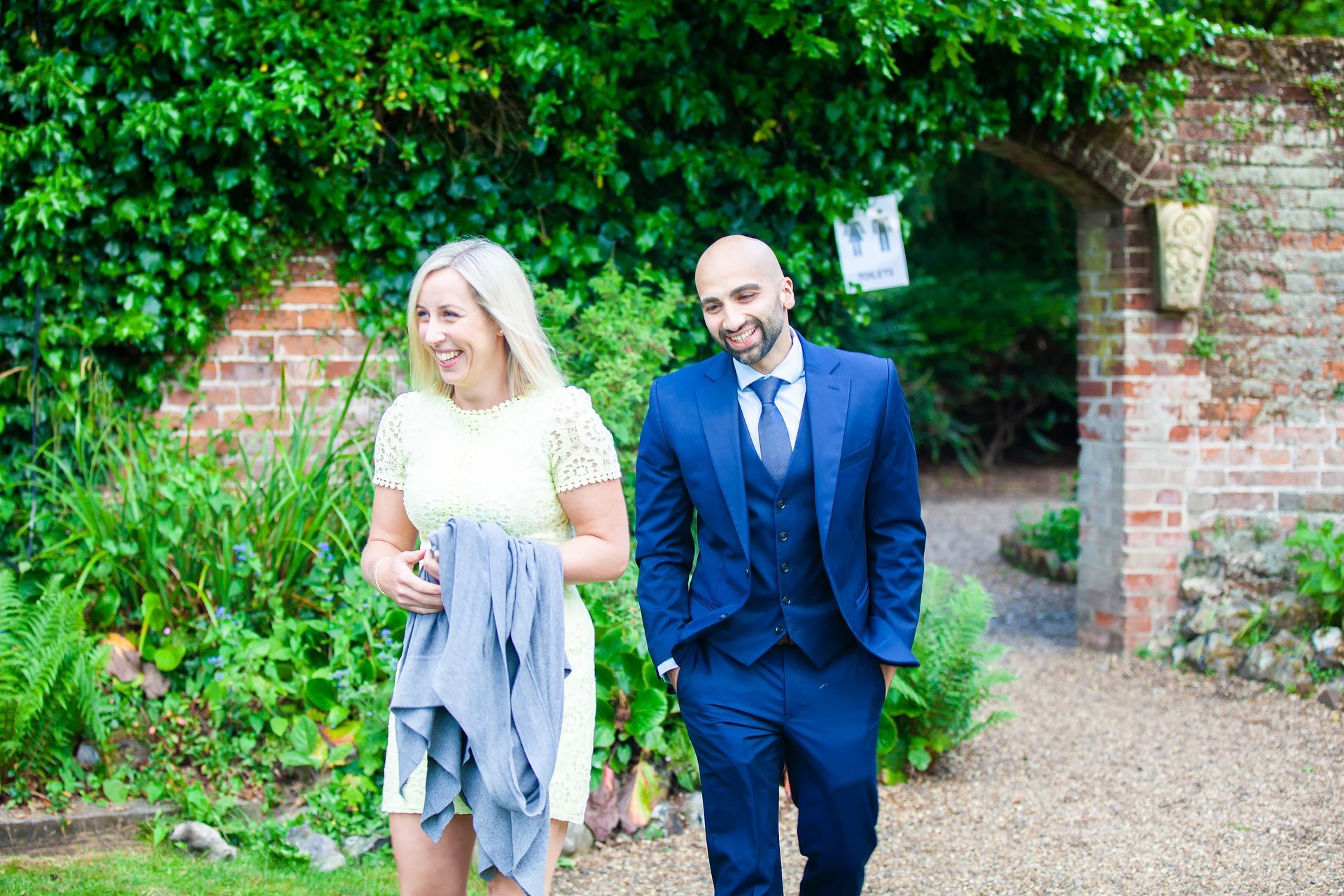 Woman in yellow dress and man in blue suit walking, smiling, in a garden.