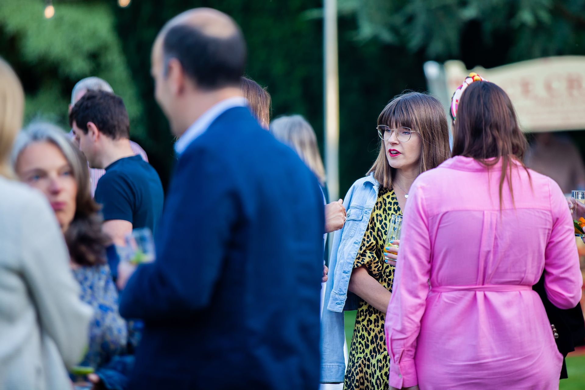 People socializing at an outdoor event: woman in leopard print dress, pink shirt, blue jacket.