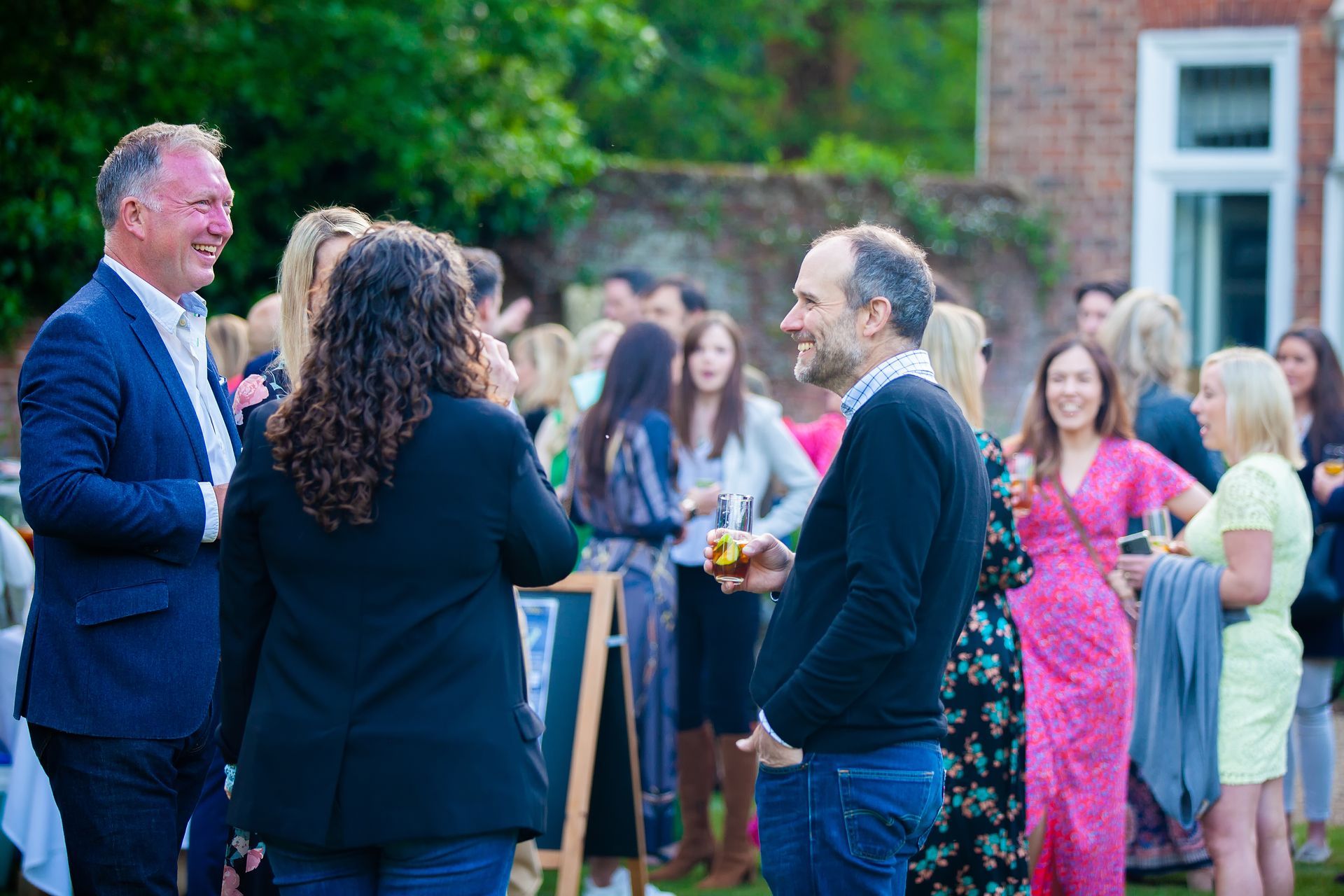 People socializing at an outdoor event, garden party; some are talking and smiling.