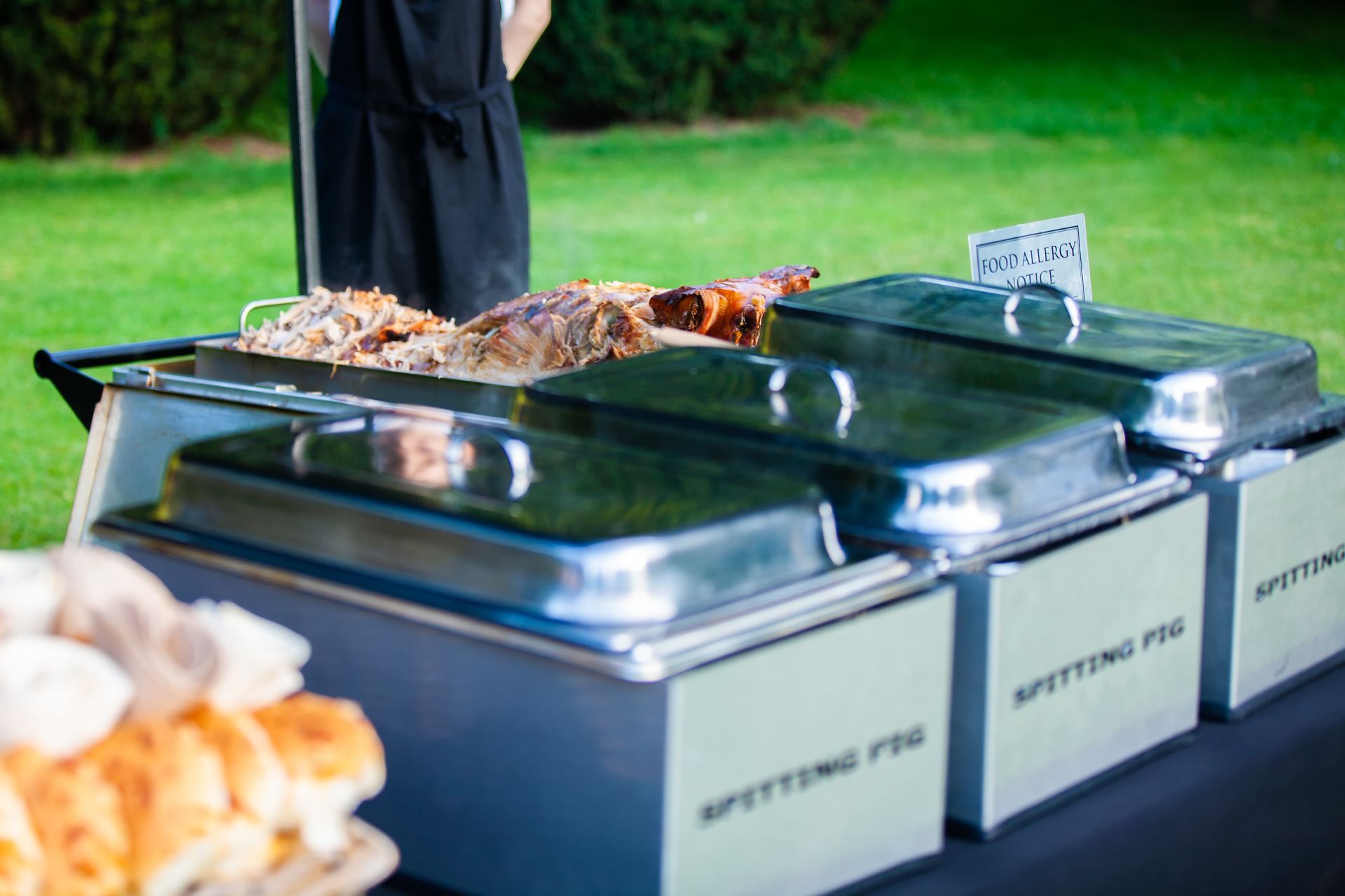 Outdoor catering buffet with roasted pig and side dishes.